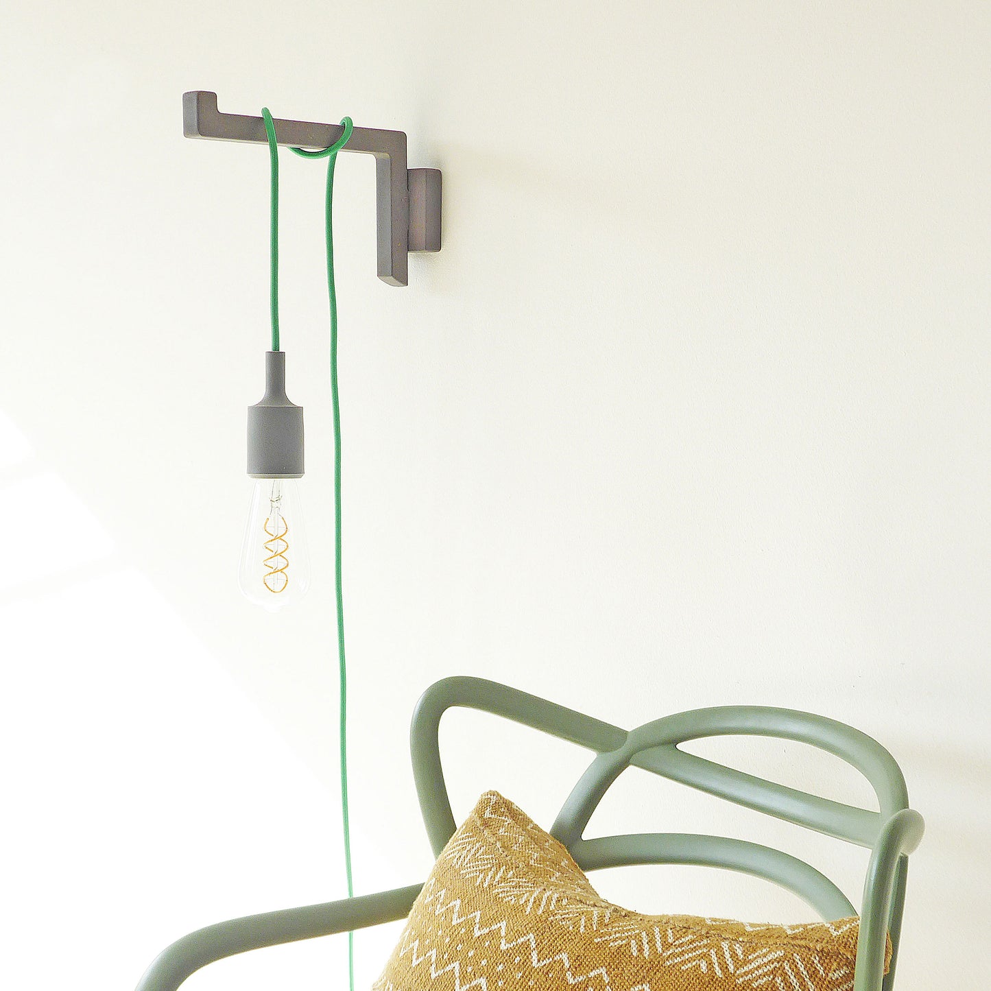 Wall-mounted wooden light bracket in grey with green plug in pendant light cord wrapped around the arm.