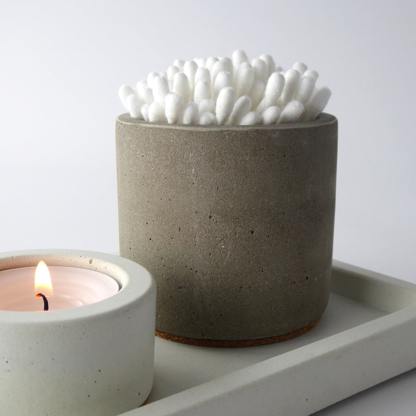 Concrete bathroom pot holding cotton buds next to a white concrete tea light holder on a matching white rectangular tray.