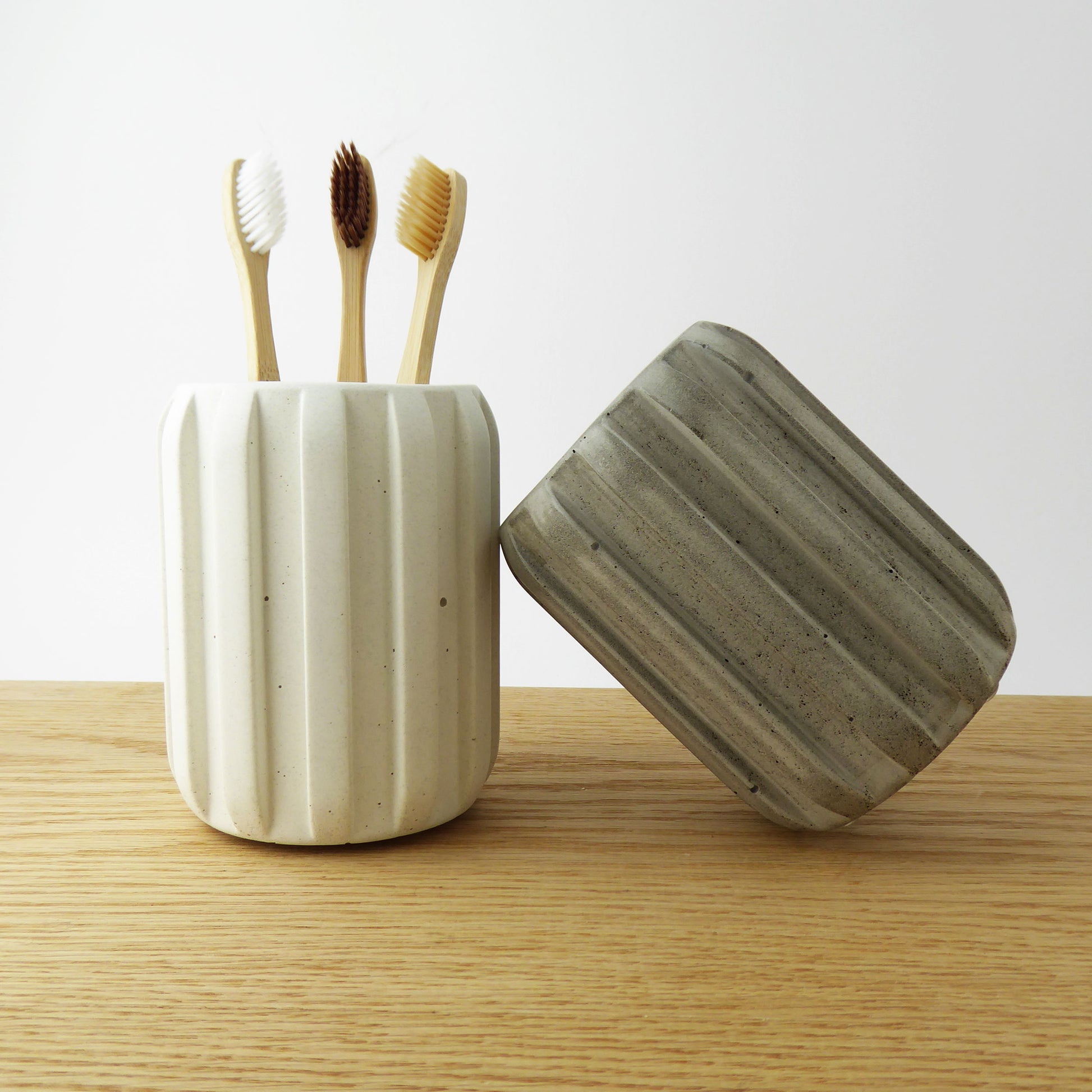 Grey and white concrete toothbrush holder with a ribbed design holding bamboo toothbrushes on a wooden shelf