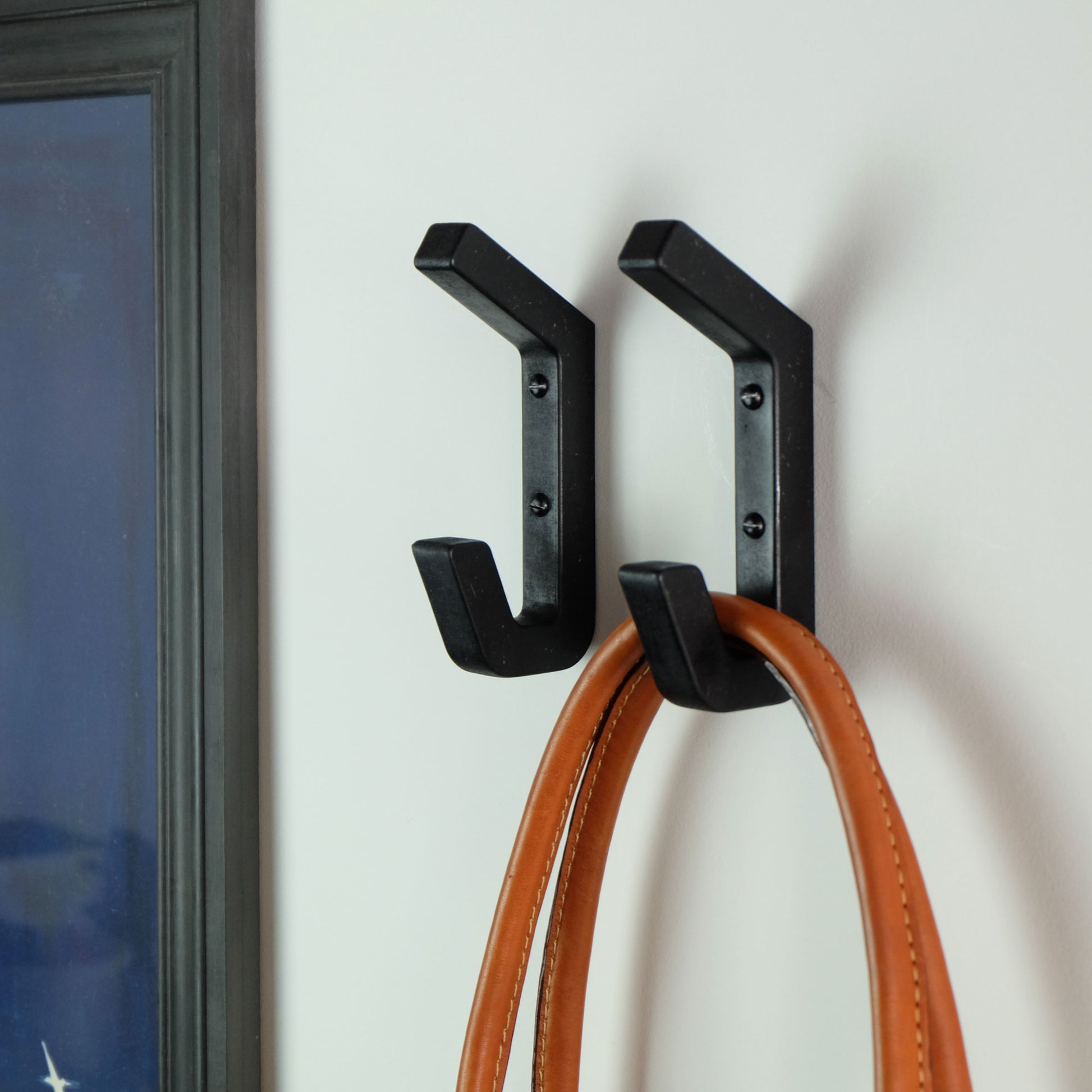 A pair of black handmade wooden wall hooks mounted in a hallway with a bah hanging from one.