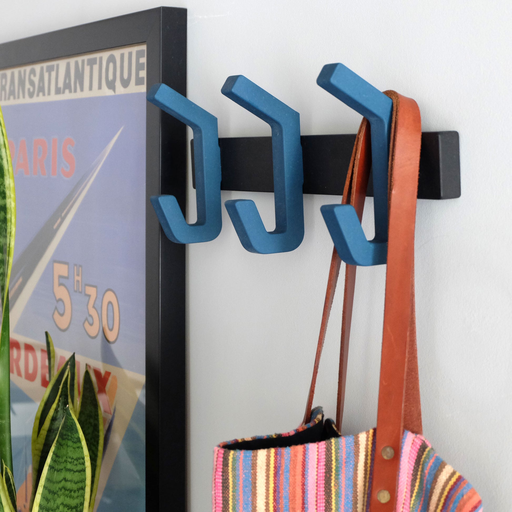 Modern blue wooden coat rack with matt black wall bracket in a hallway with a beach bag hanging from one of the hooks