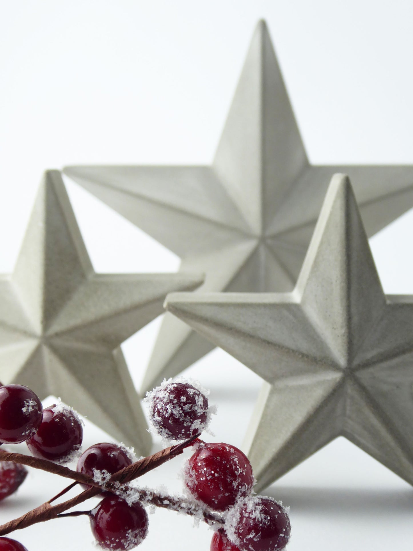 Three star-shaped decorative ornaments with a branch of red festive berries in the foreground.