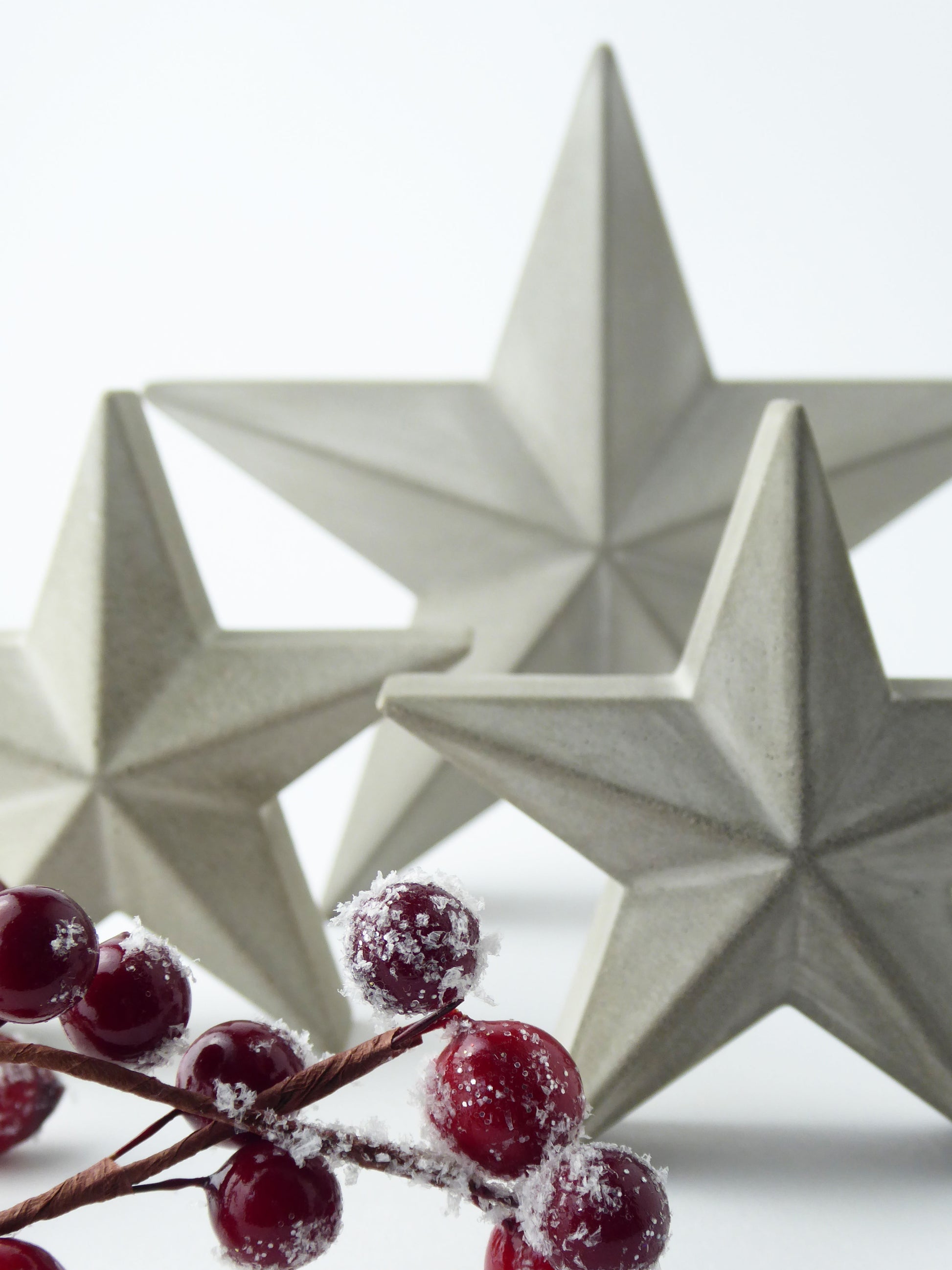 Three star-shaped decorative ornaments with a branch of red festive berries in the foreground.