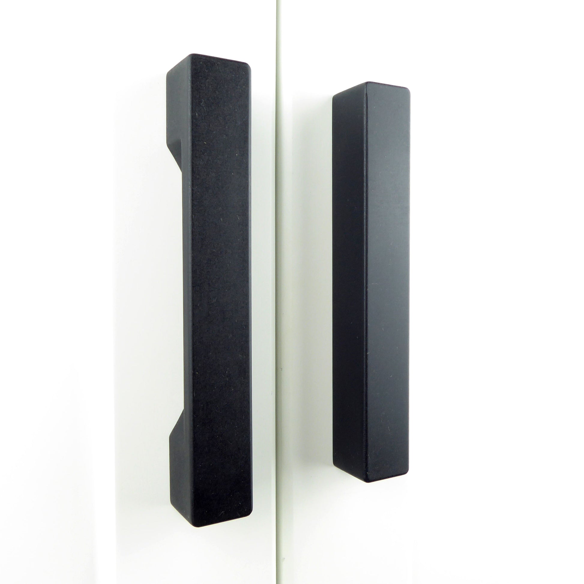 A pair of black, chunky wooden drawer pulls crafted from black eco-friendly Valchromat wood installed on a white wardrobe doors.