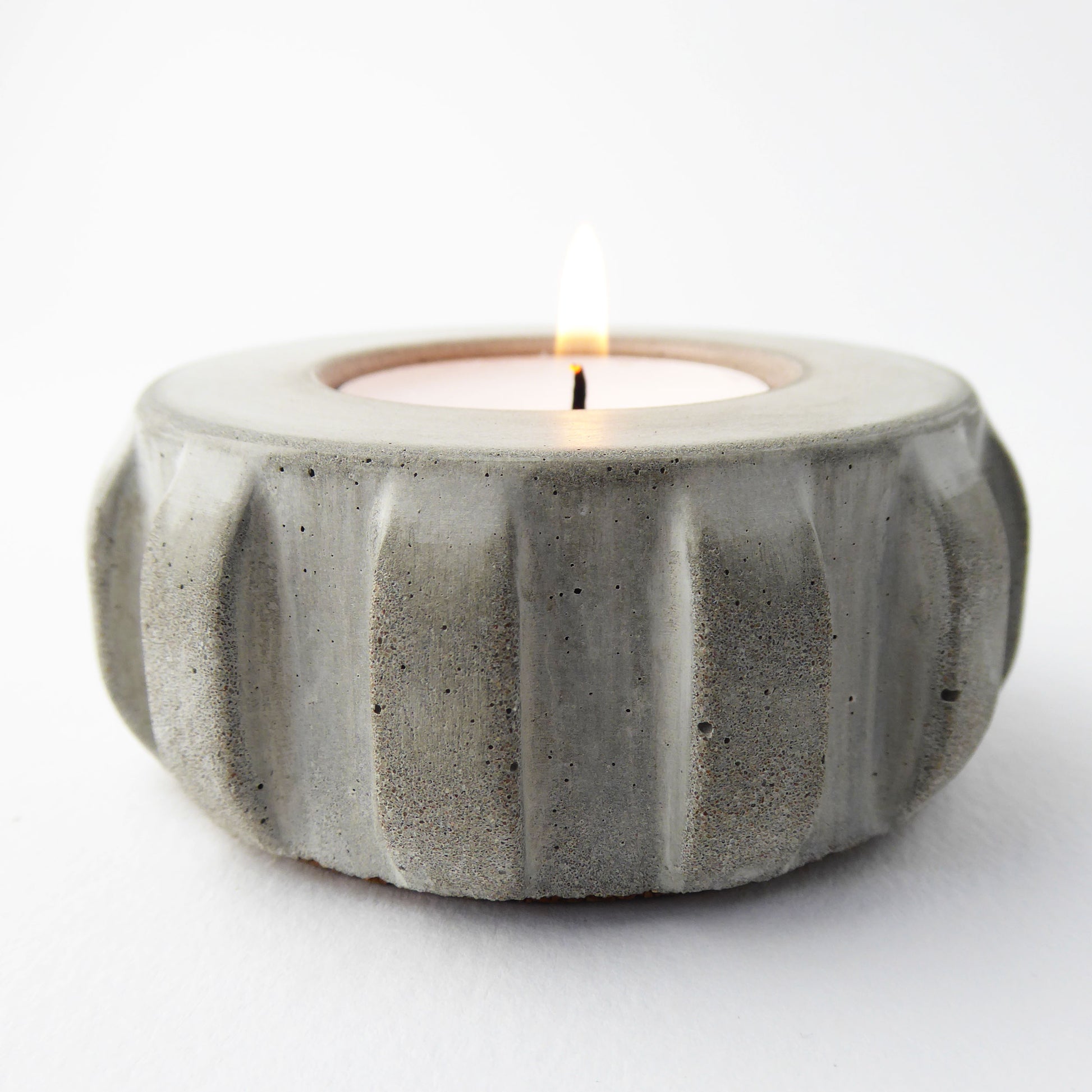 Natural concrete candle holder with a lit candle on a white background