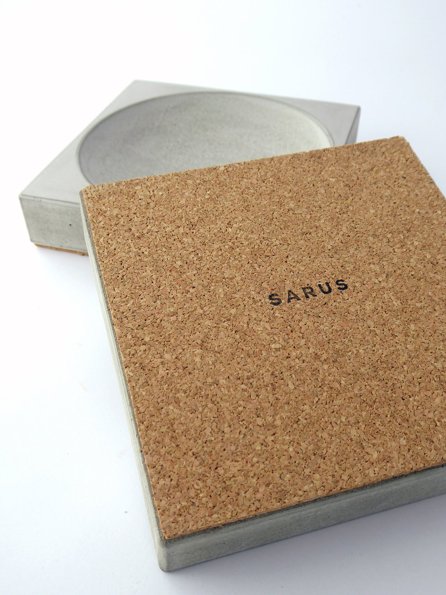 Square raw concrete with a cork base and printed SARUS logo