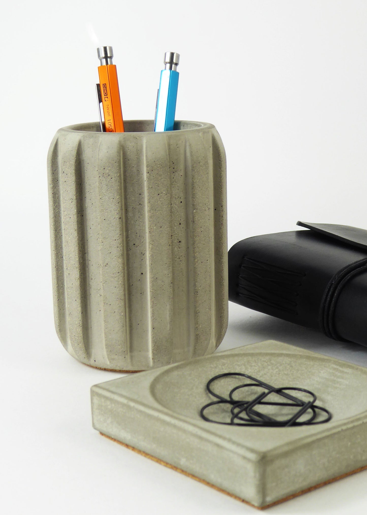Raw concrete desk accessories - a pen pot, a small square tray holding paperclips and a leather notebook