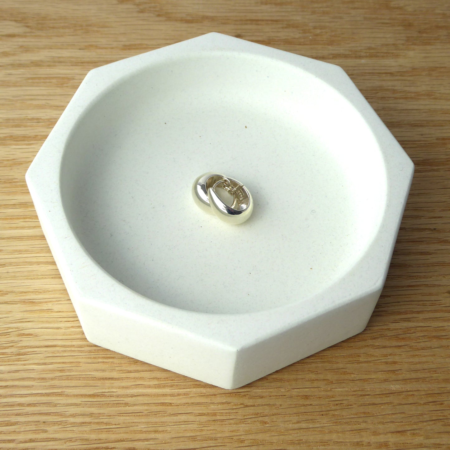 White concrete bowl holding jewellery on a bedside table.