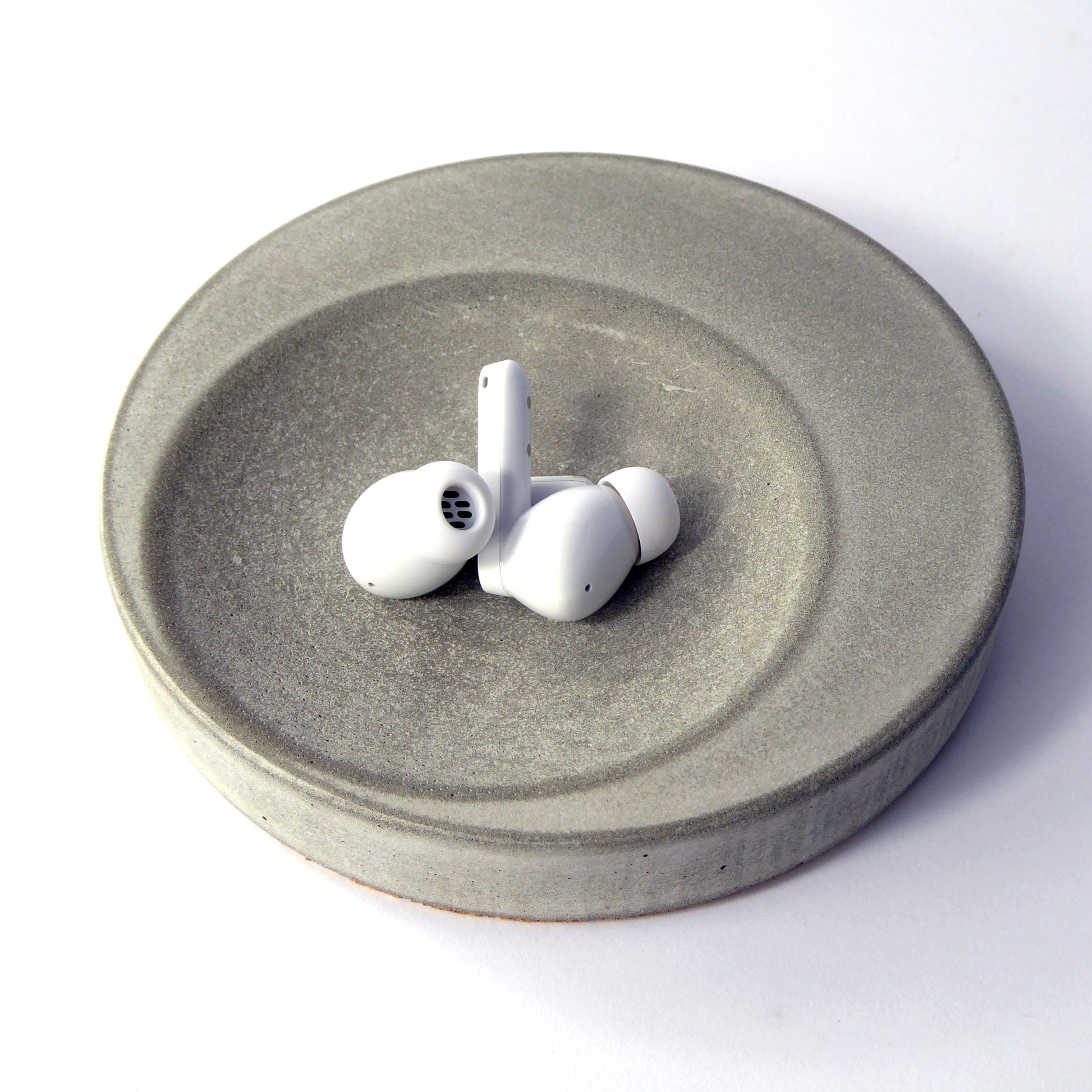 A small round concrete decorative tray in natural grey colour, displayed with a pair of ear pods on top, placed against a white background.