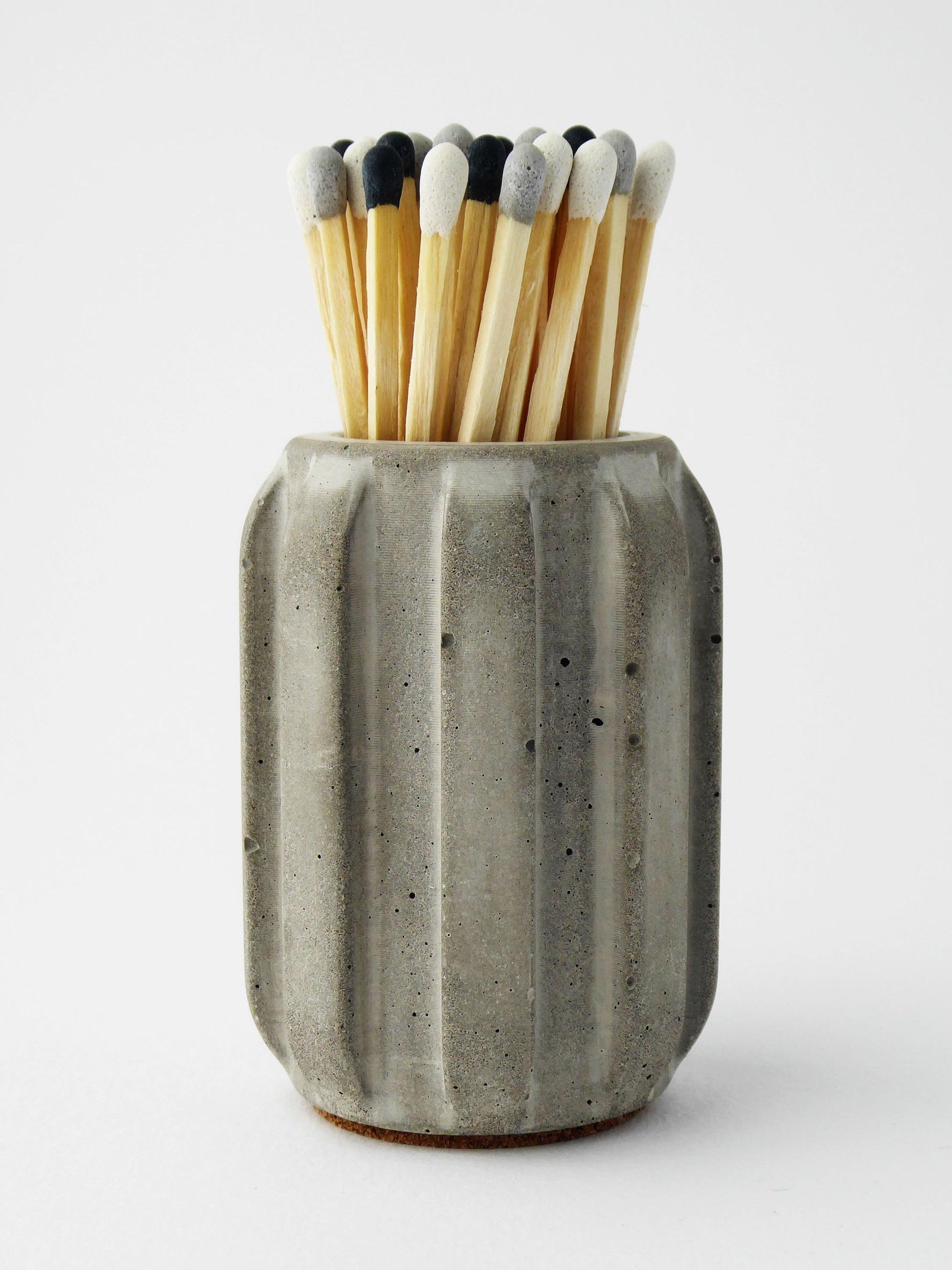 Grey concrete match pot holder with long coloured matches on a white background