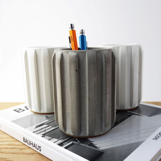 Raw concrete pen holder with colourful pens on a book on a wooden shekf