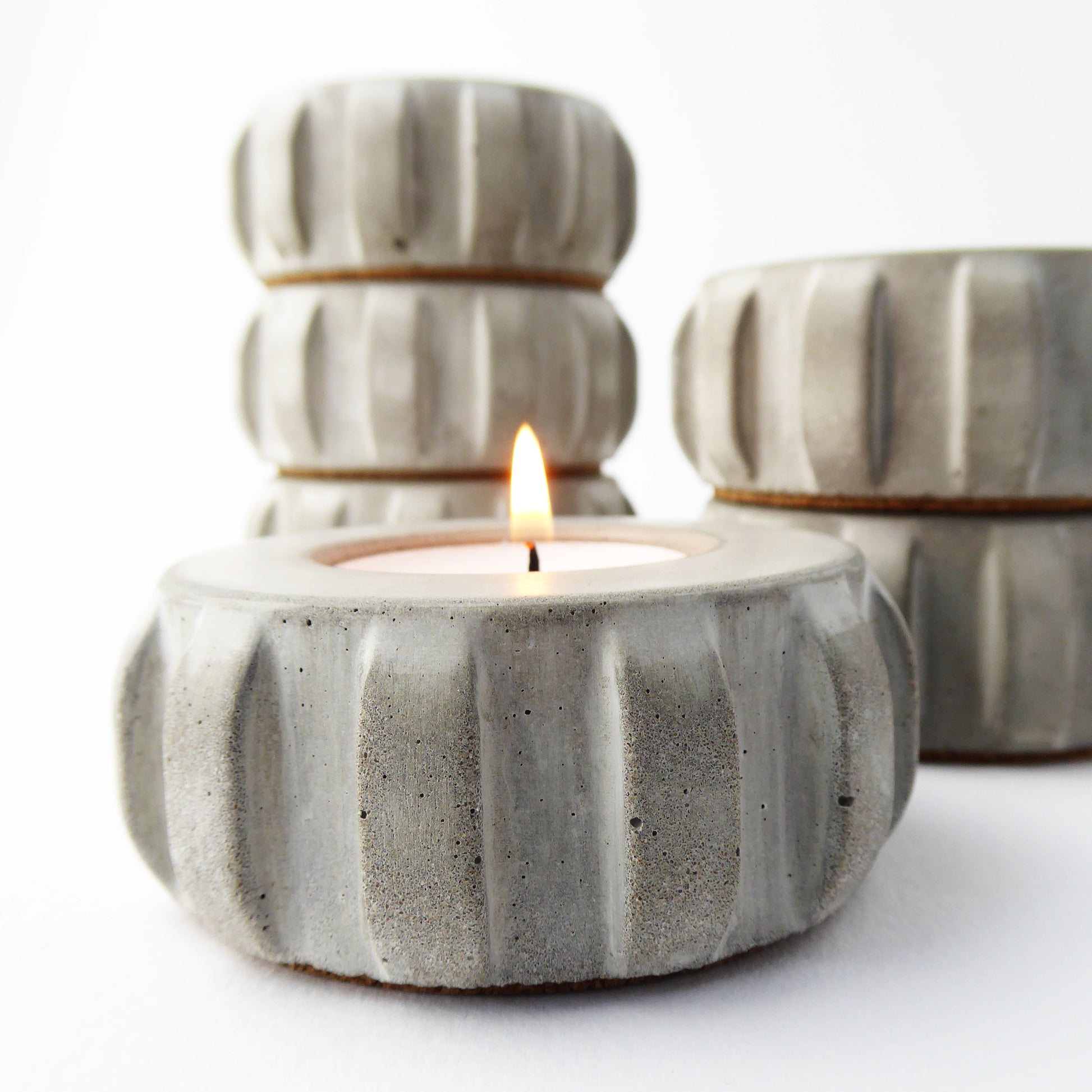 Grey concrete candle holder with a lit candle on a white background