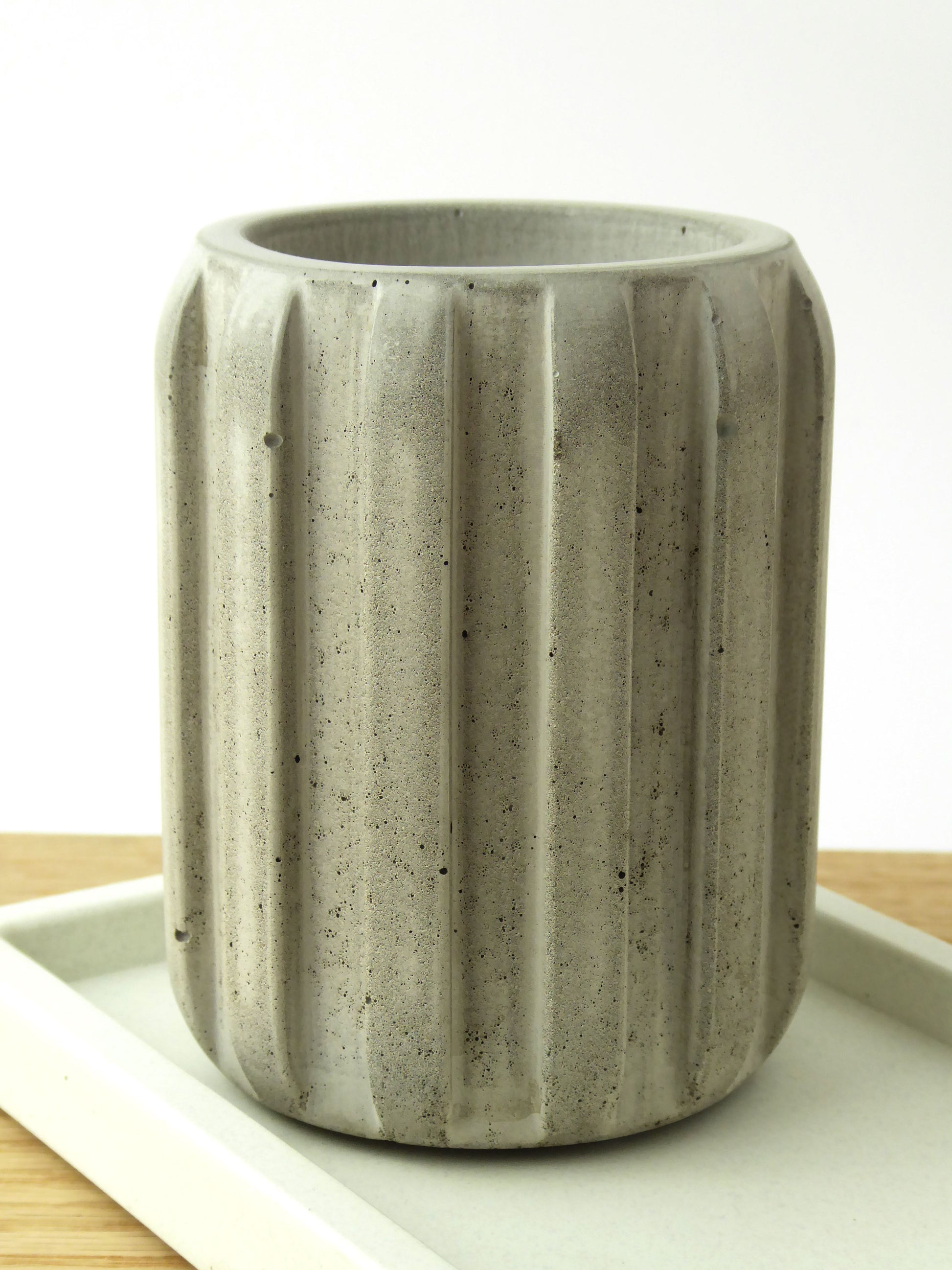 Raw grey concrete pot with a striped ribbed design on a white concrete tray with a light background