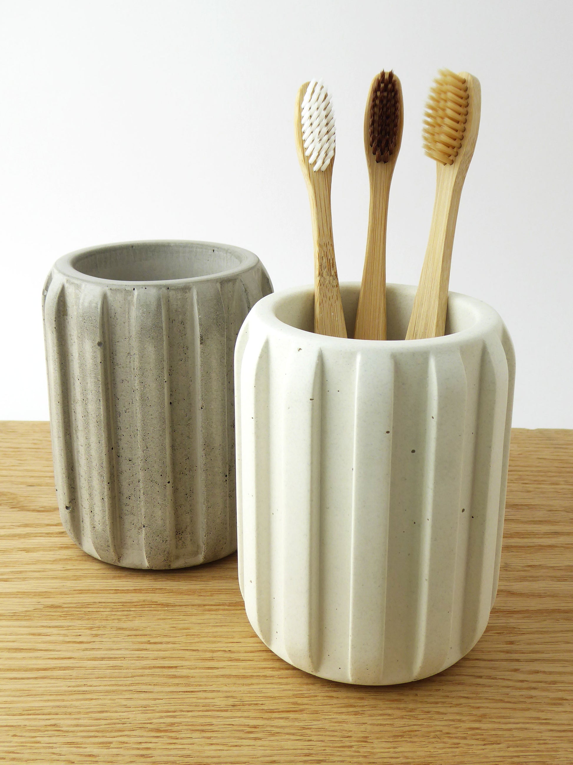 Two ceramic toothbrush holders with wooden toothbrushes on a wooden shelf.