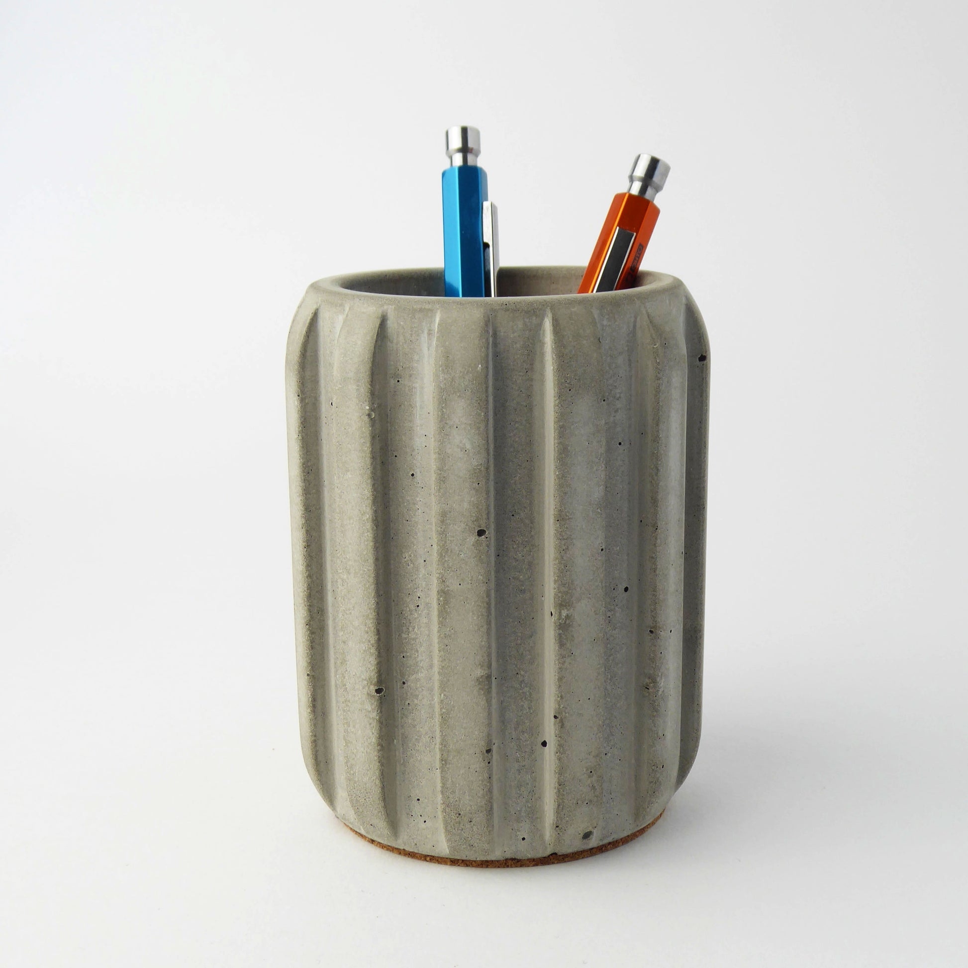 Concrete pen holder with a ribbed design with two colourful pens on a white background.