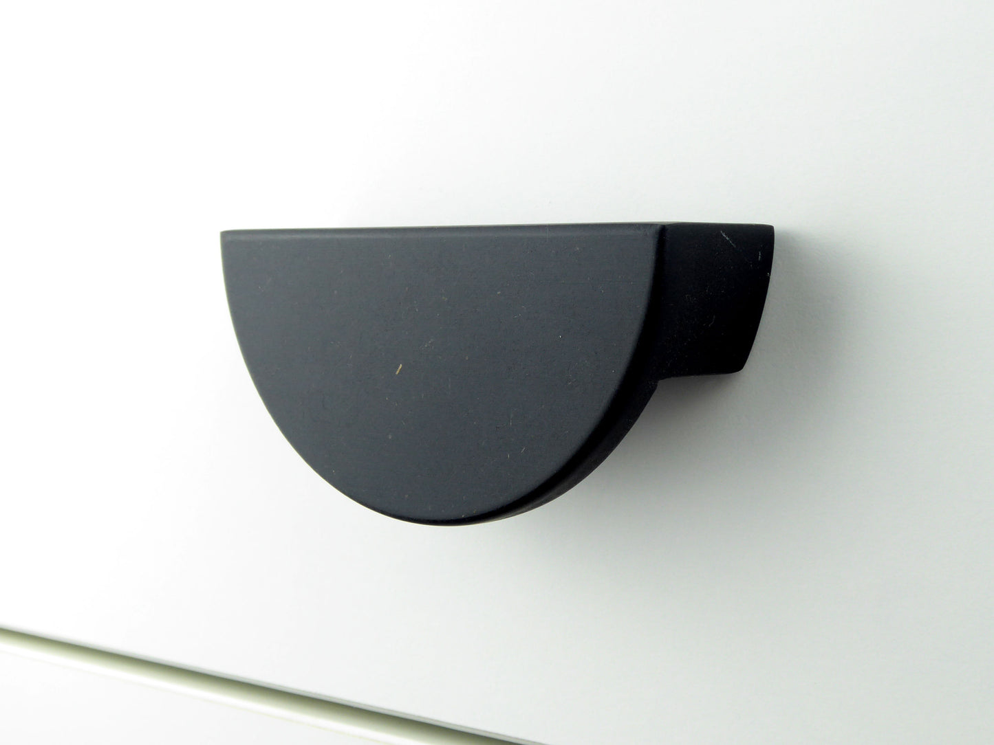 A handmade drawer handle in a half moon shape made from black Valchromat wood