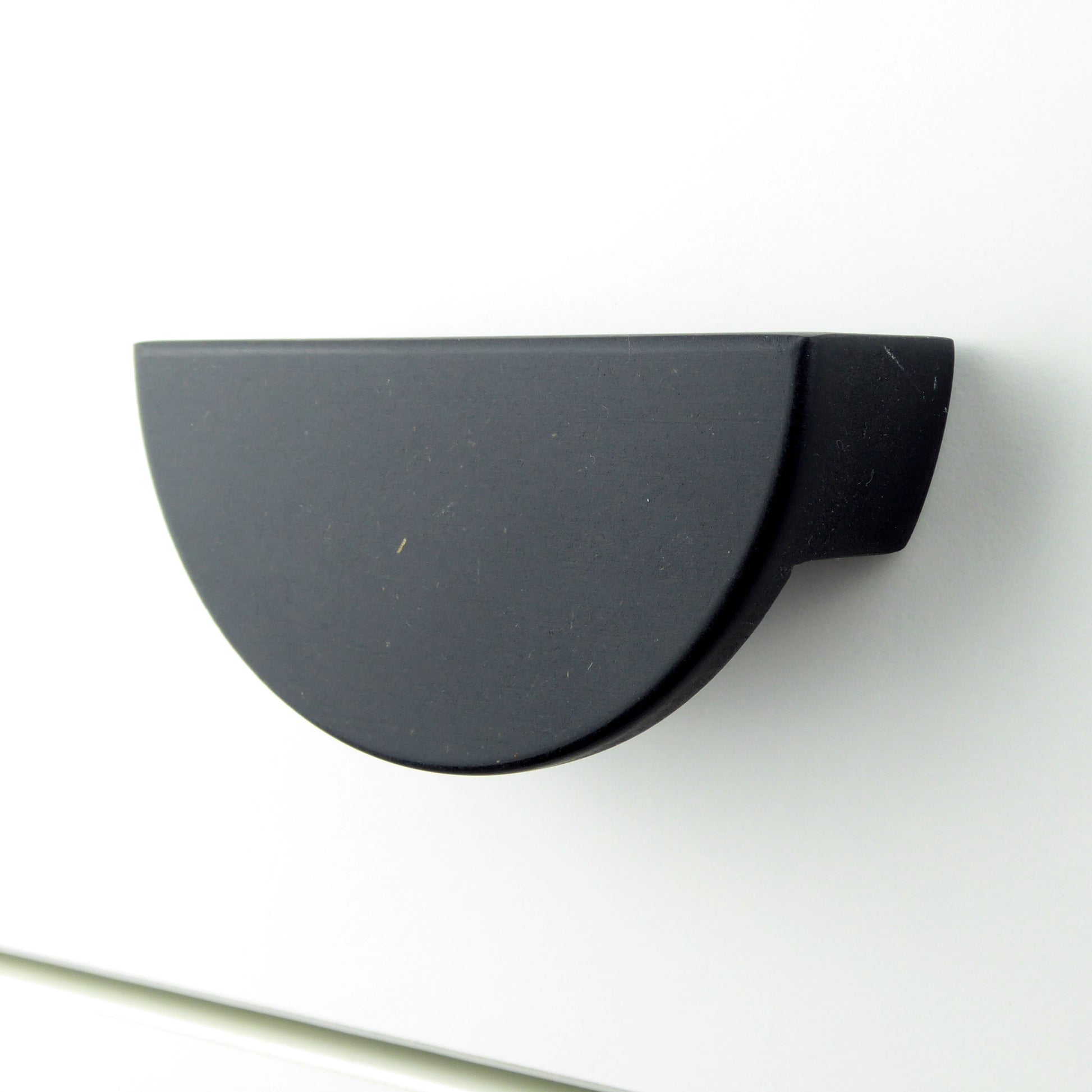 A half moon shaped matte black wooden cabinet knob mounted on a white drawer.