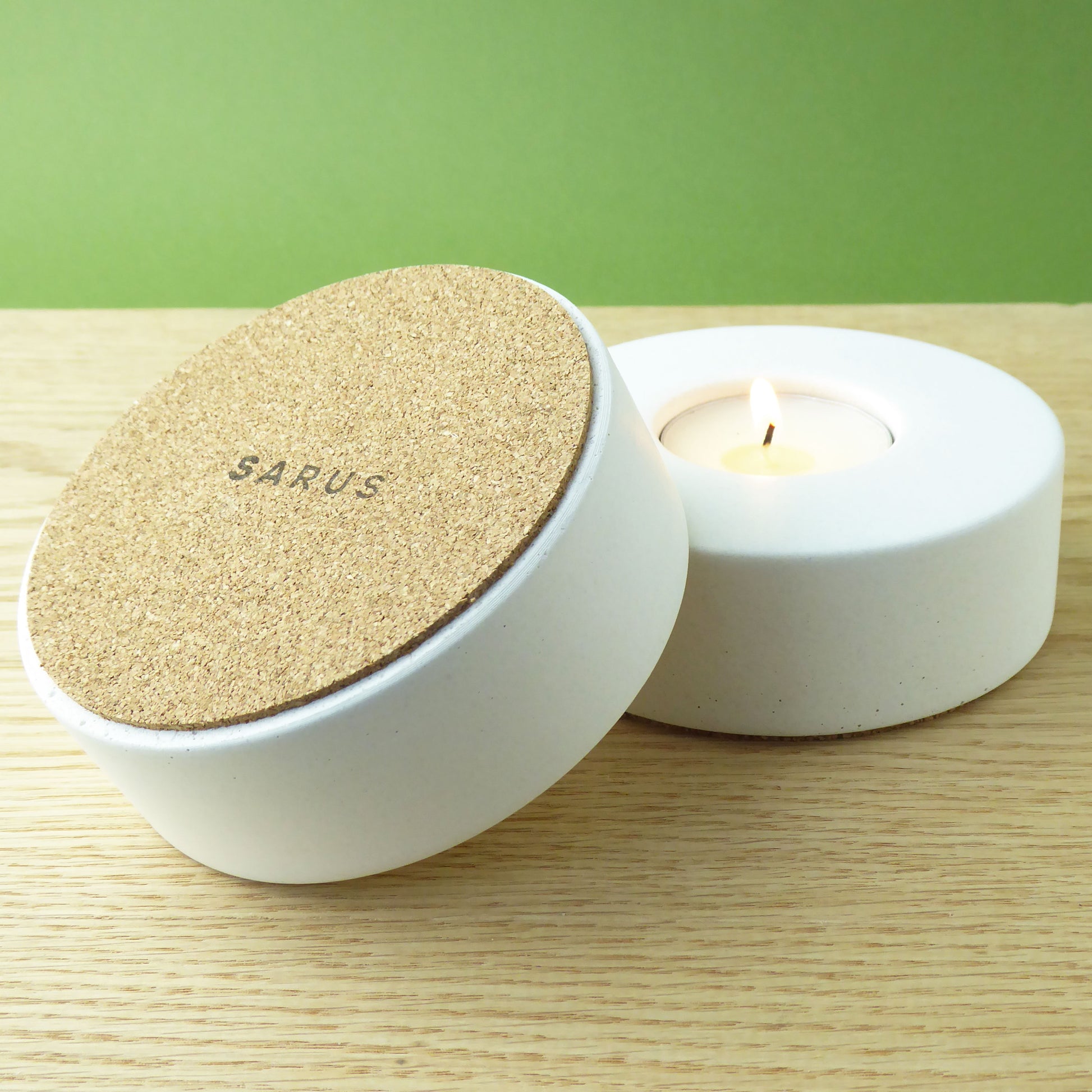 Modern white candle holder with a lit tea light inside and another candle holder showing the cork base to protect surfaces