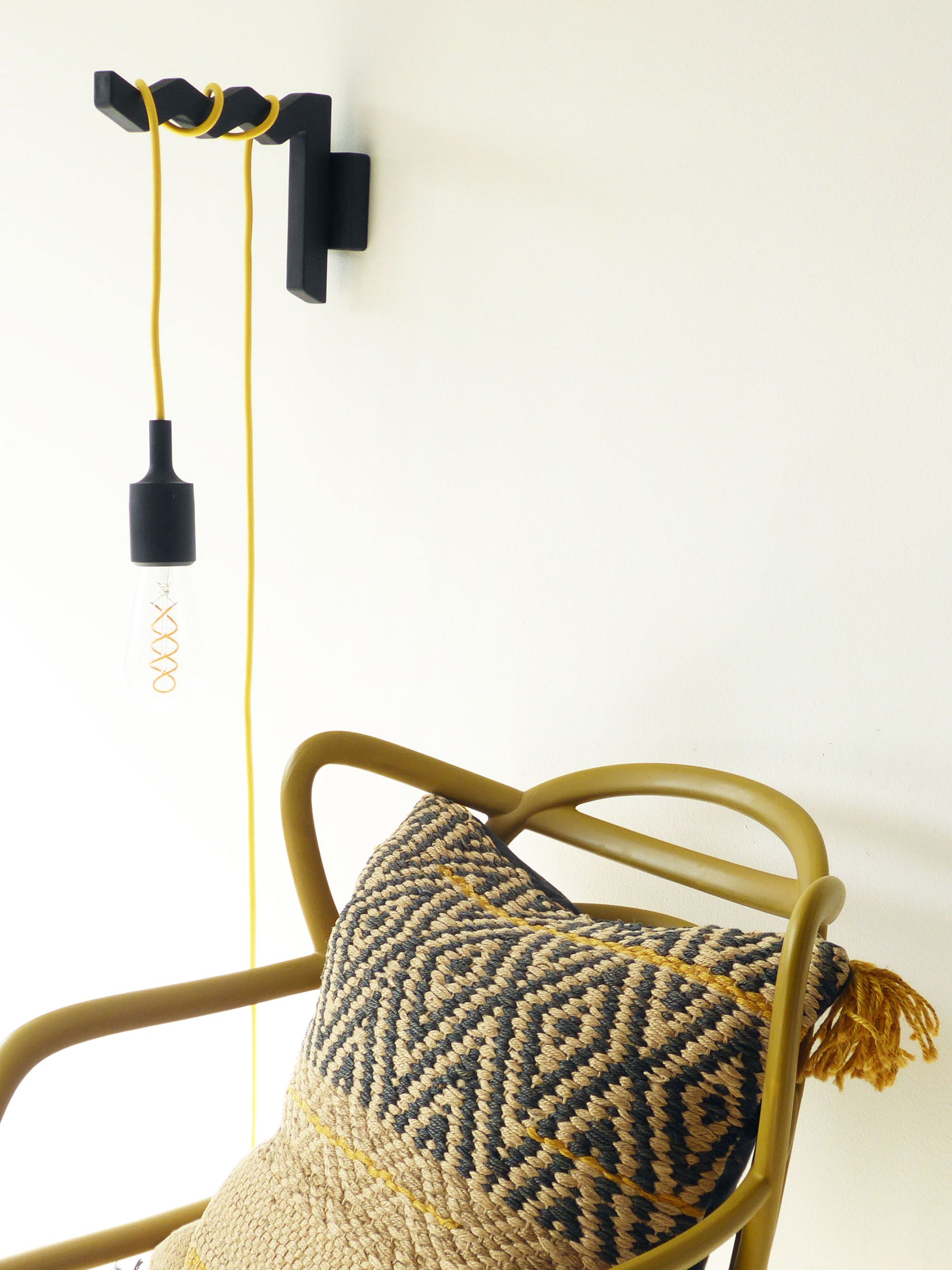 wall-mounted lamp hook with a yellow cord pendant light wrapped around the arm positioned as a reading light above a chair