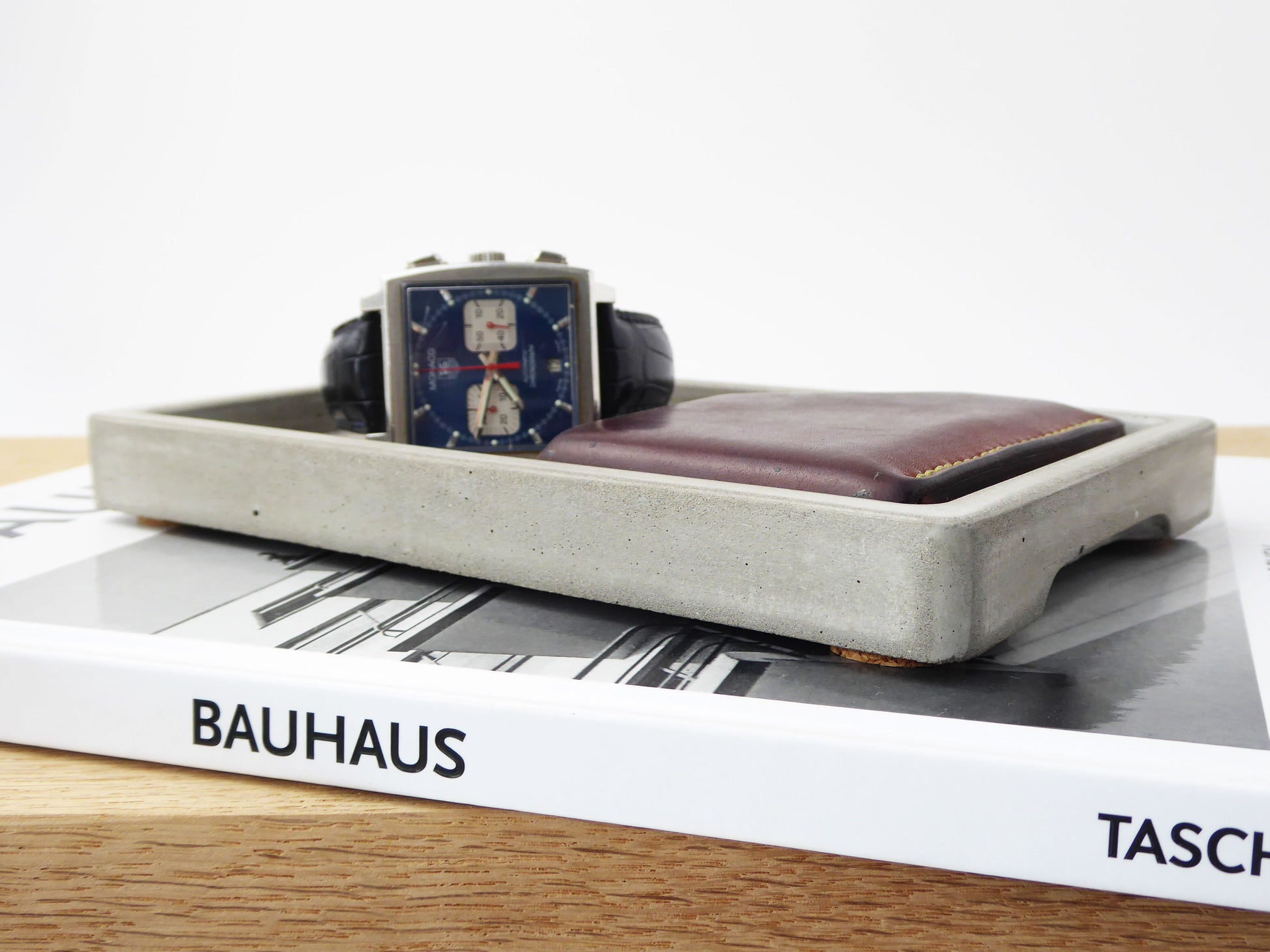 Natural grey concrete tray with a mens watch and leather wallet on a bedside table