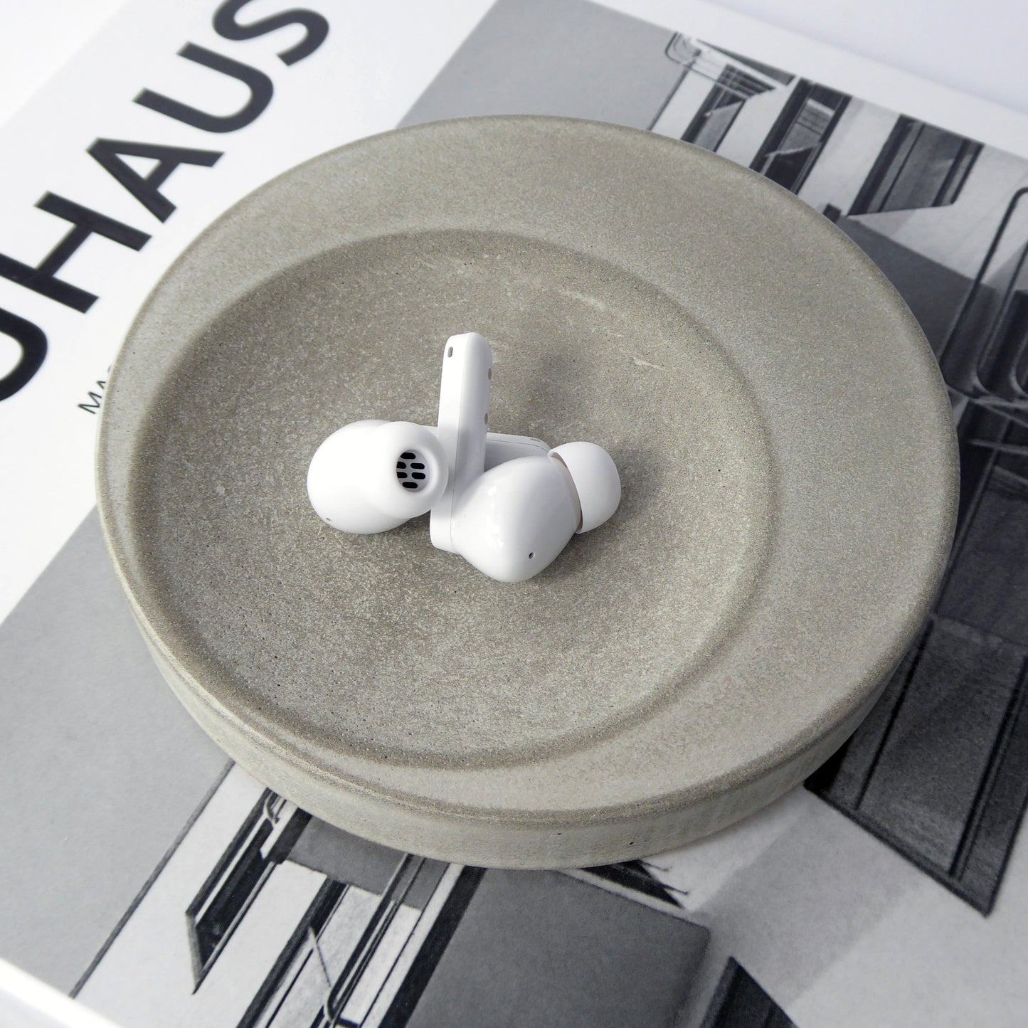 Round trinket tray in natural grey concrete holding a pair of ear pods on a book