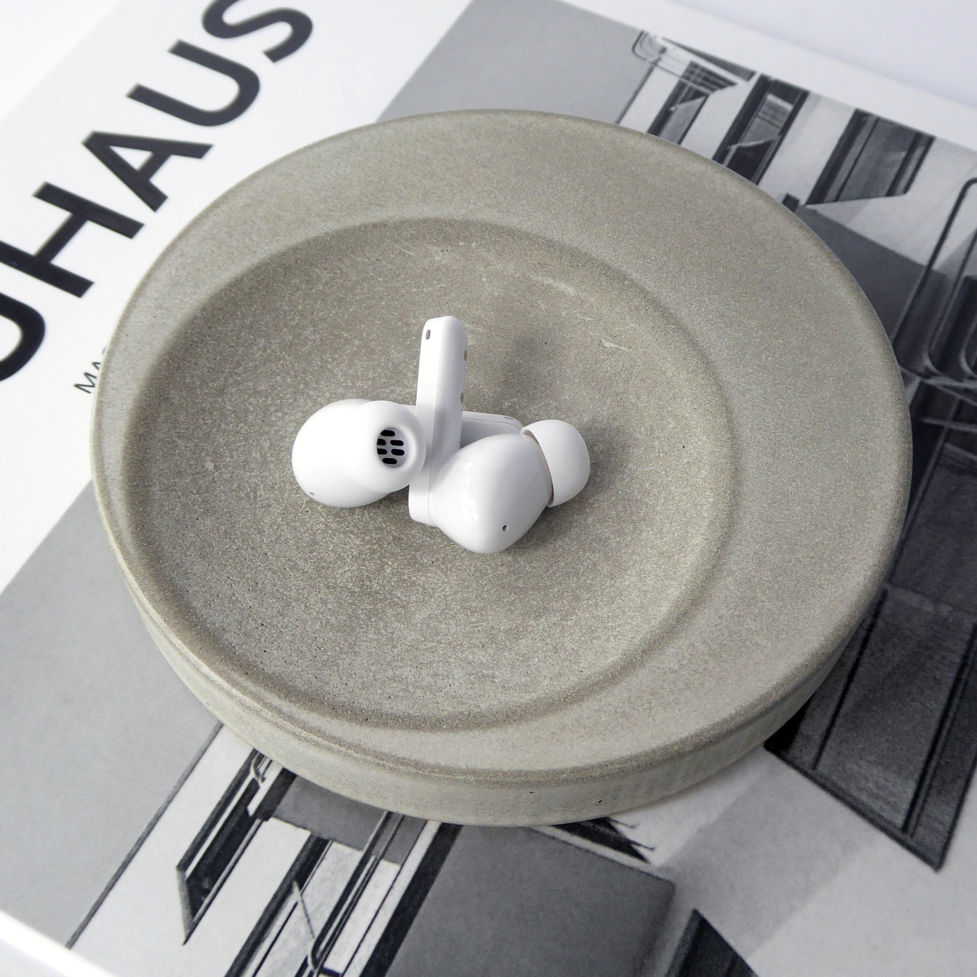 Round trinket tray in natural grey concrete holding a pair of ear pods on a book