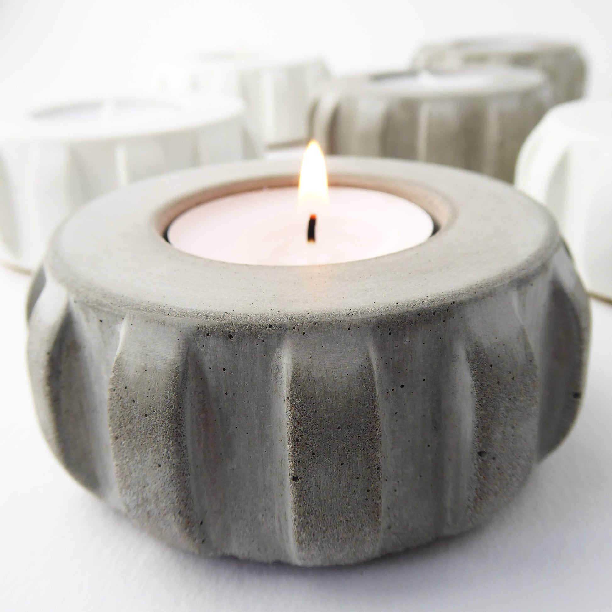Grey concrete candle holder with a lit tea light inside on a white background