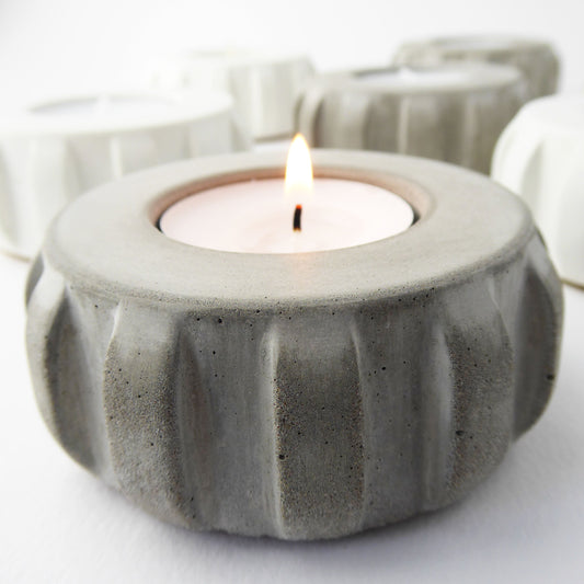 Grey concrete candle holder with a lit tea light inside on a white background