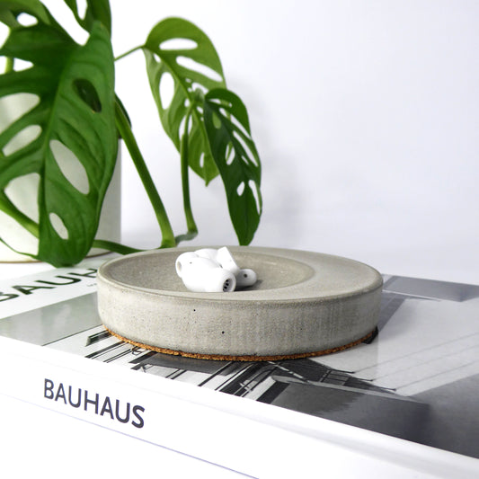Round concrete dish with white wireless ear pods on a book with a plant in the background