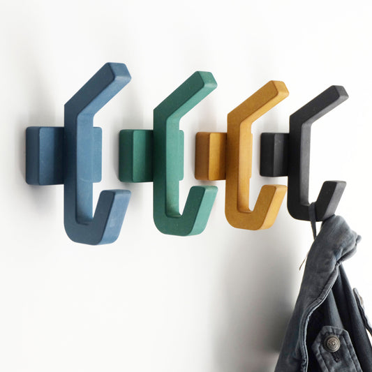 A set of handcrafted wooden wall hooks in black, blue, green, and yellow, displayed on a white wall with a jacket hanging on one of the hooks.