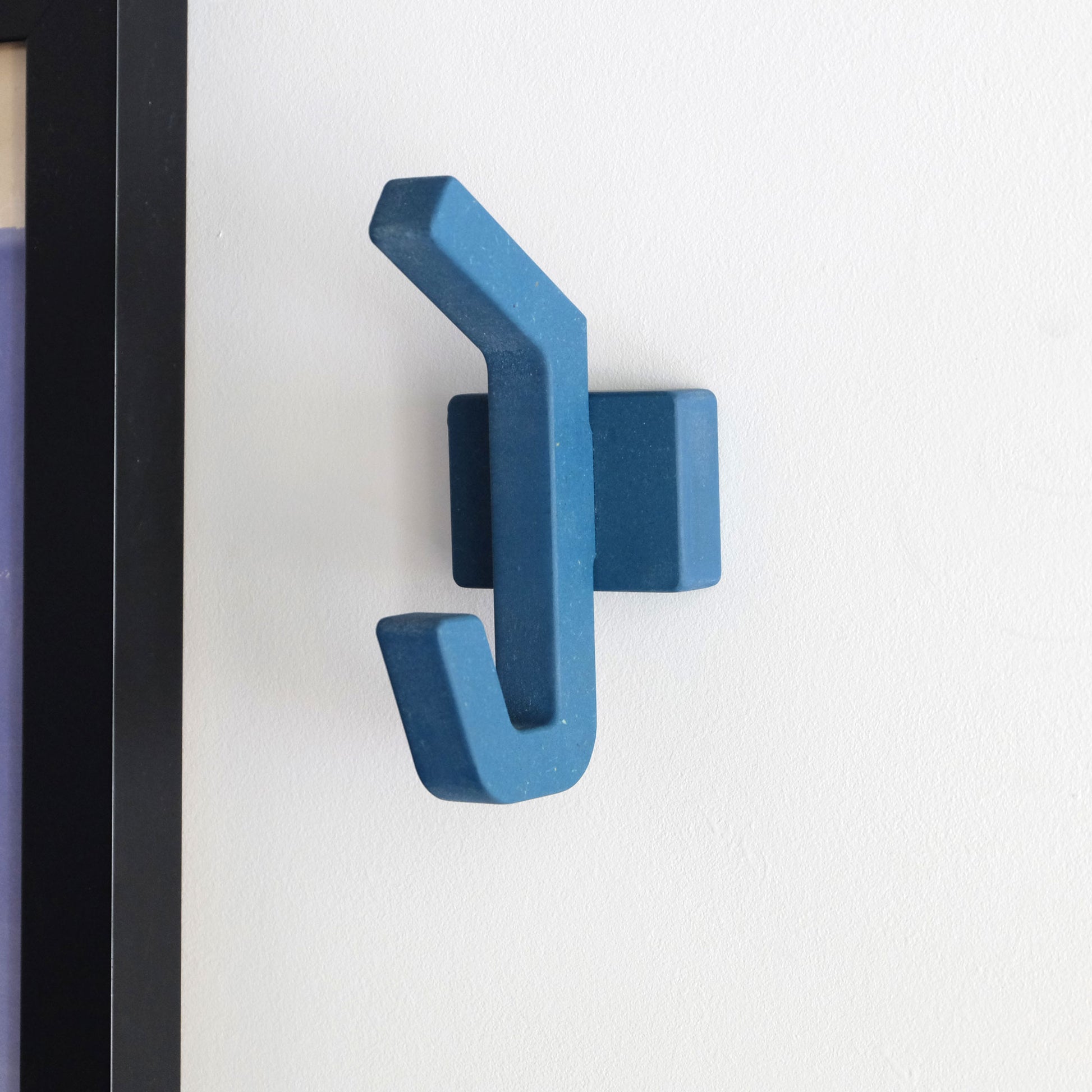 A modern blue wooden wall mounted clothes hook on a white wall.