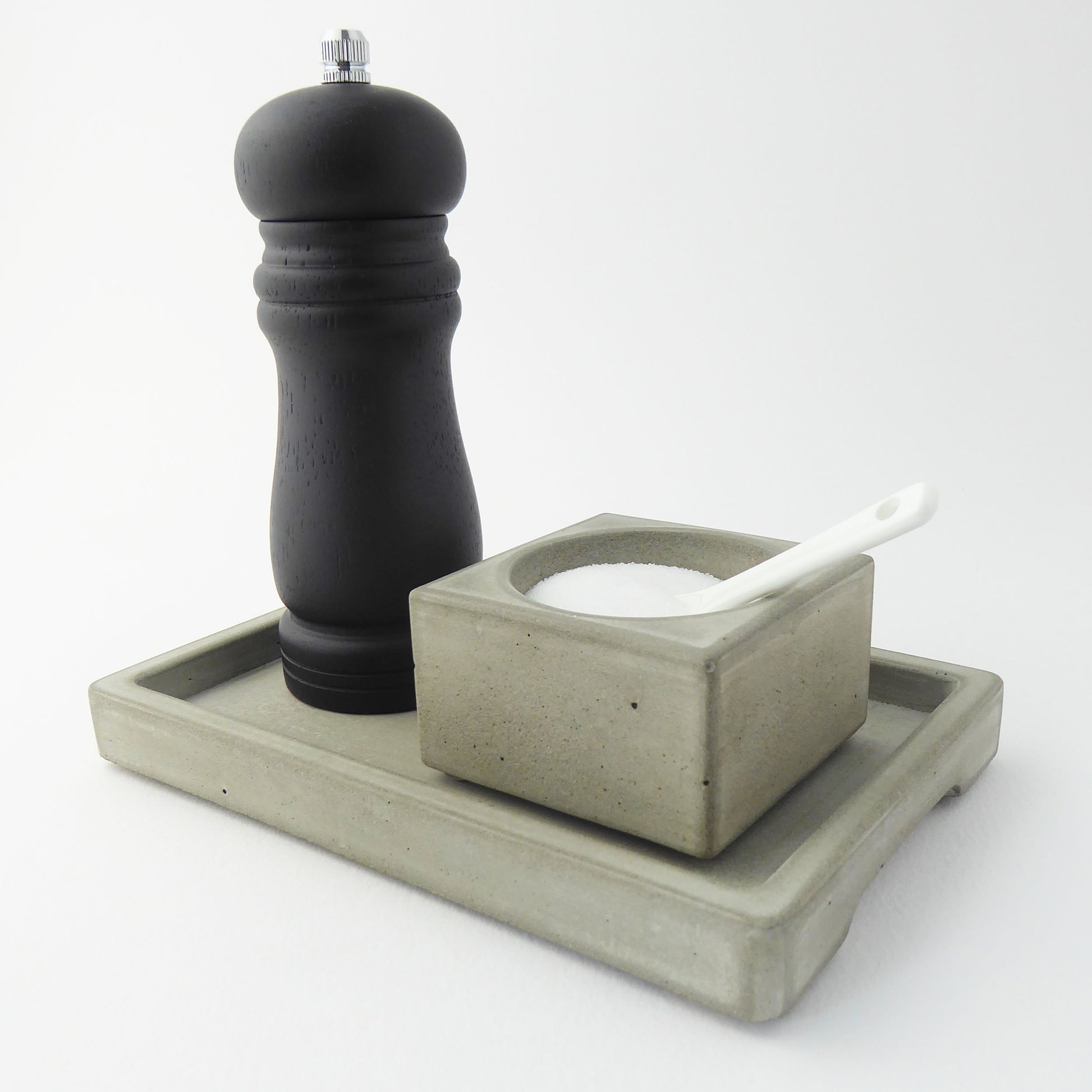 Black peppermill and grey concrete bowl containing seasalt on a matching grey concrete rectangular tray