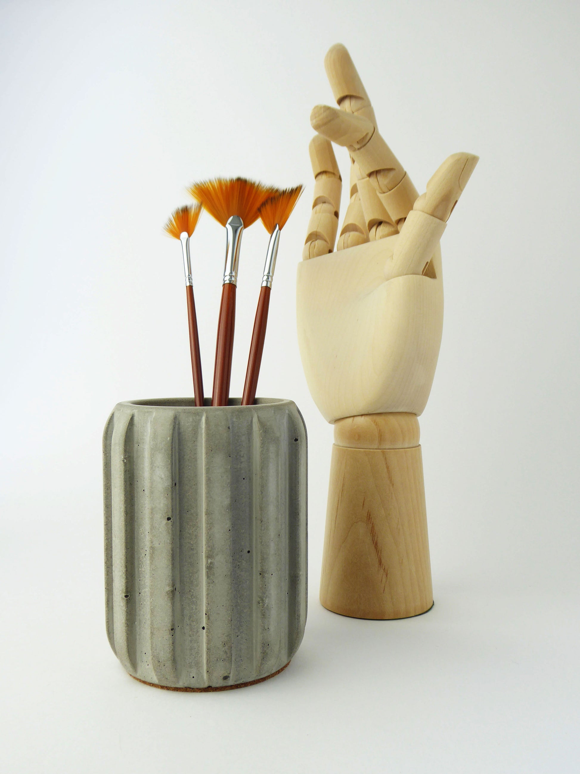 Grey concrete pot with paintbrushes and a wooden drawing hand on a white background