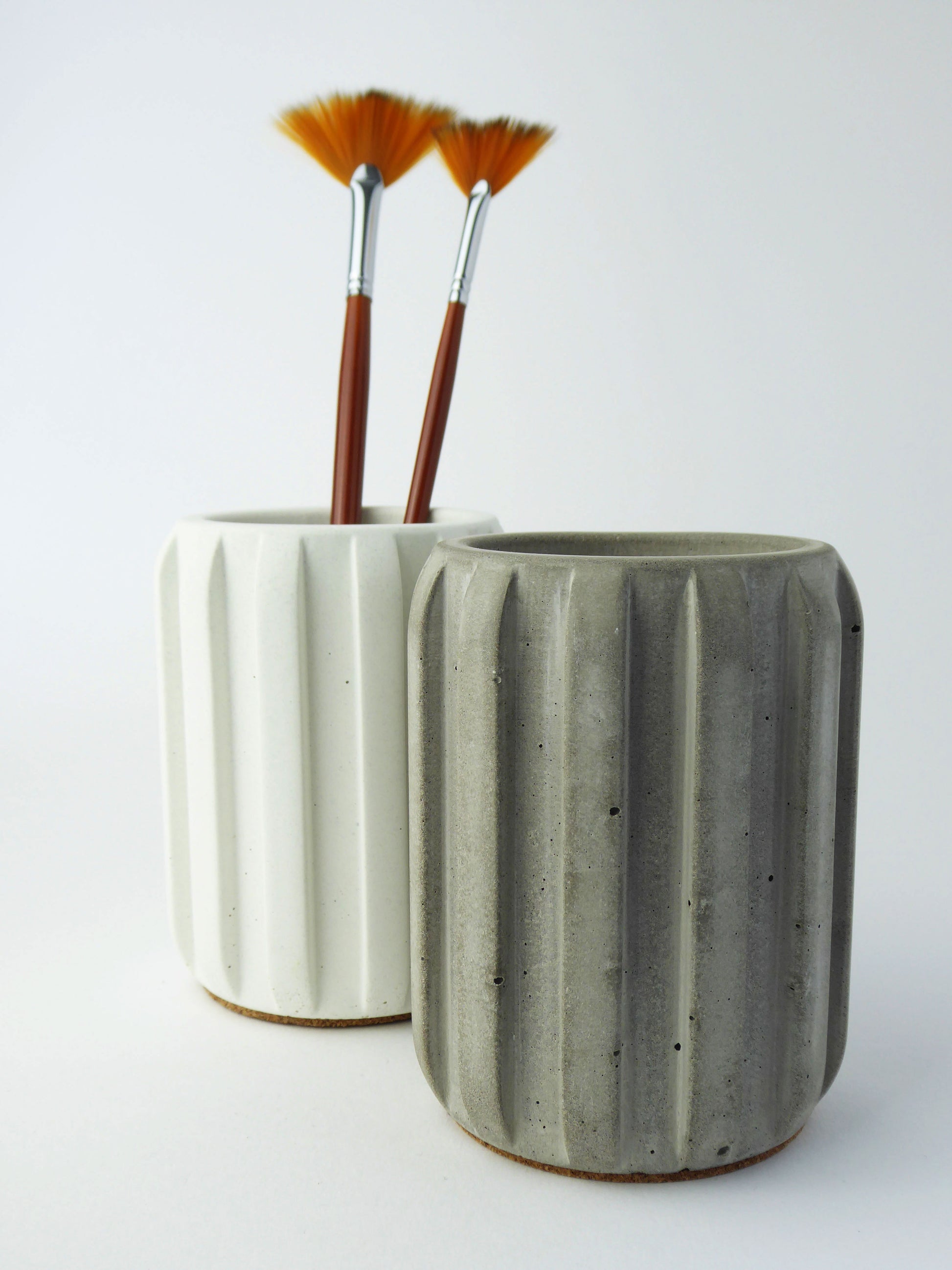 Two ceramic pots, one white and one grey, holding paintbrushes on a white background