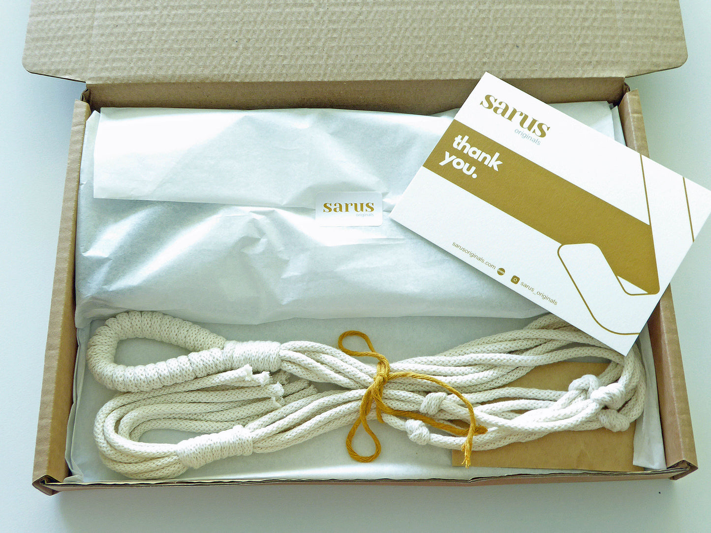 Gift box showing a tissue wrapped plant bracket and handmade macarme hanger for mothers day