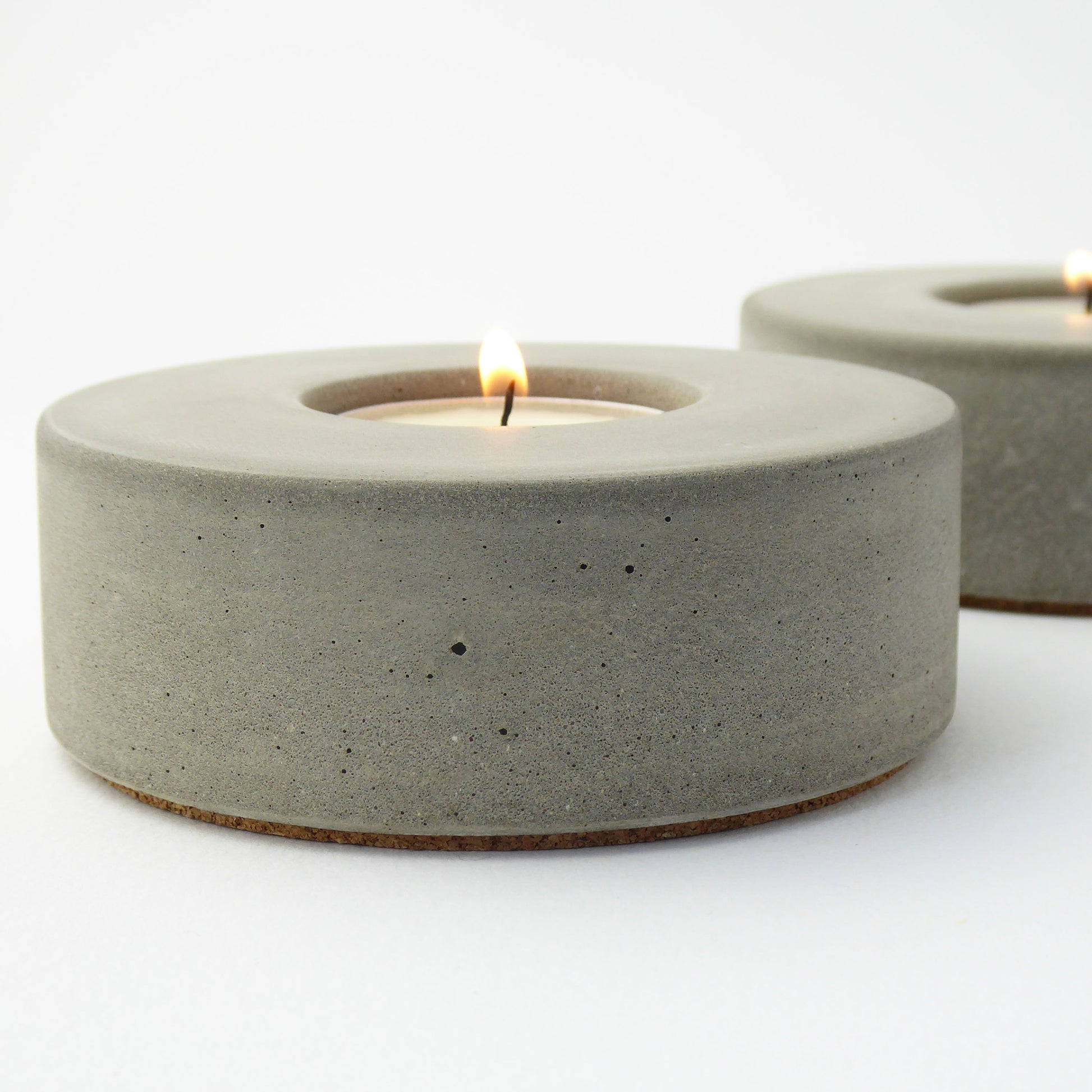 Raw concrete candle holders with lit tea lights on a white background