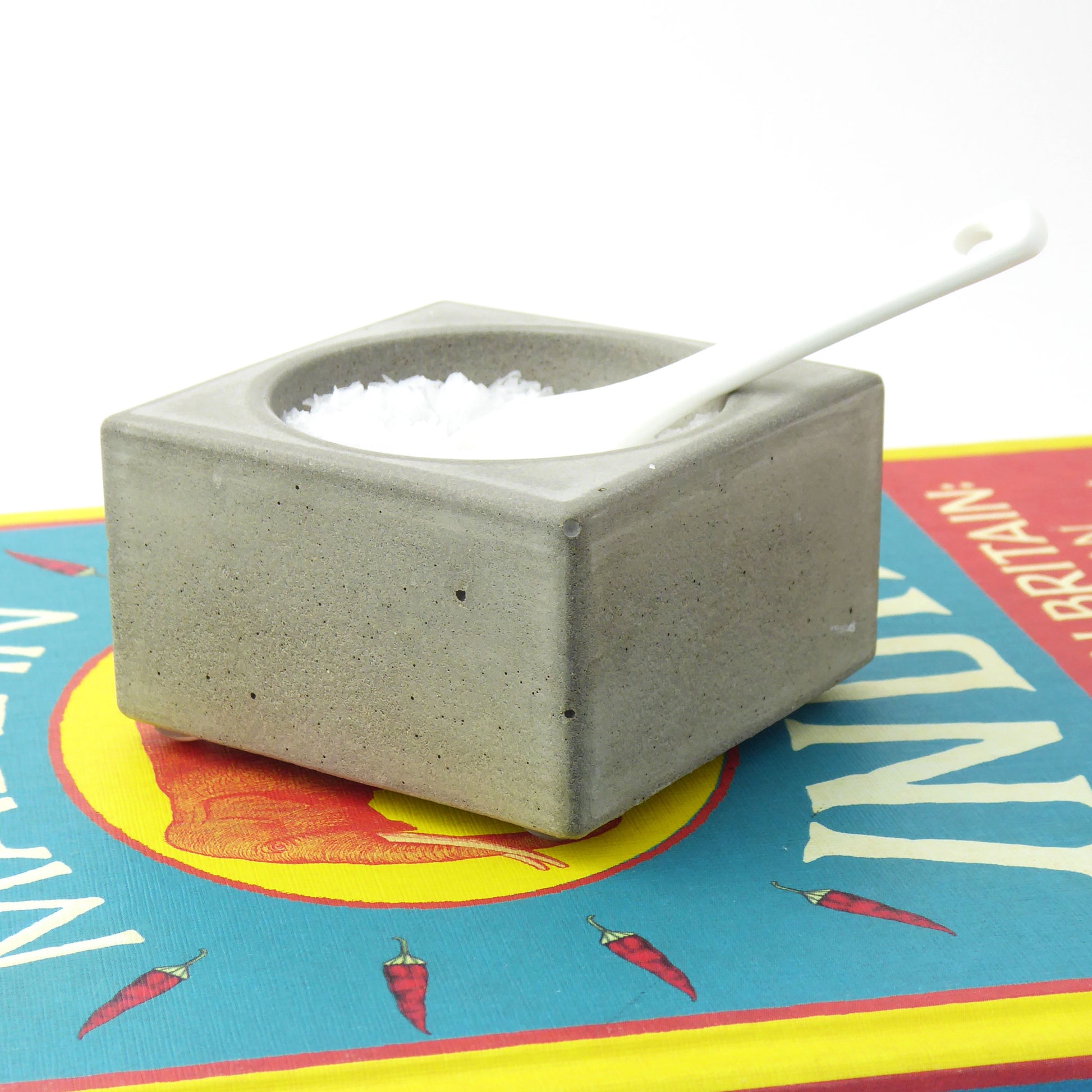 Concrete salt cellar with a white spoon on a colourful tablecloth