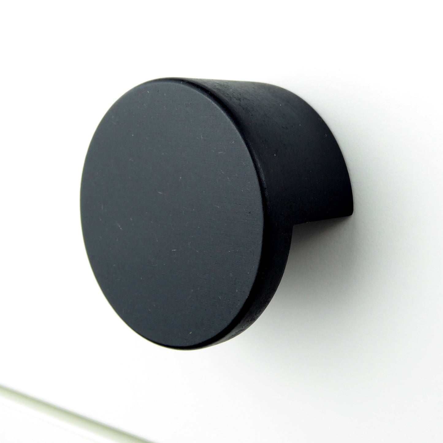 A minimalist round wooden drawer pull in matte black colour on a white cabinet