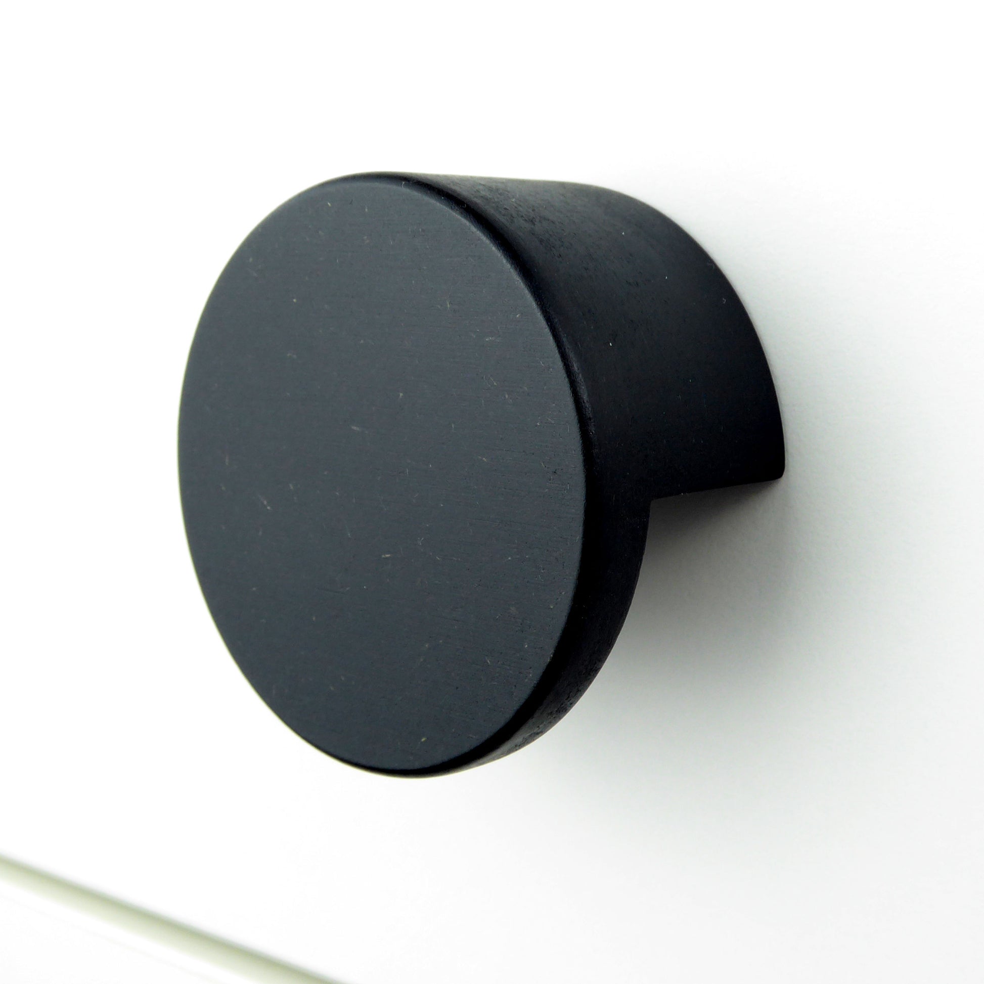 A minimalist round wooden drawer pull in matte black colour on a white cabinet