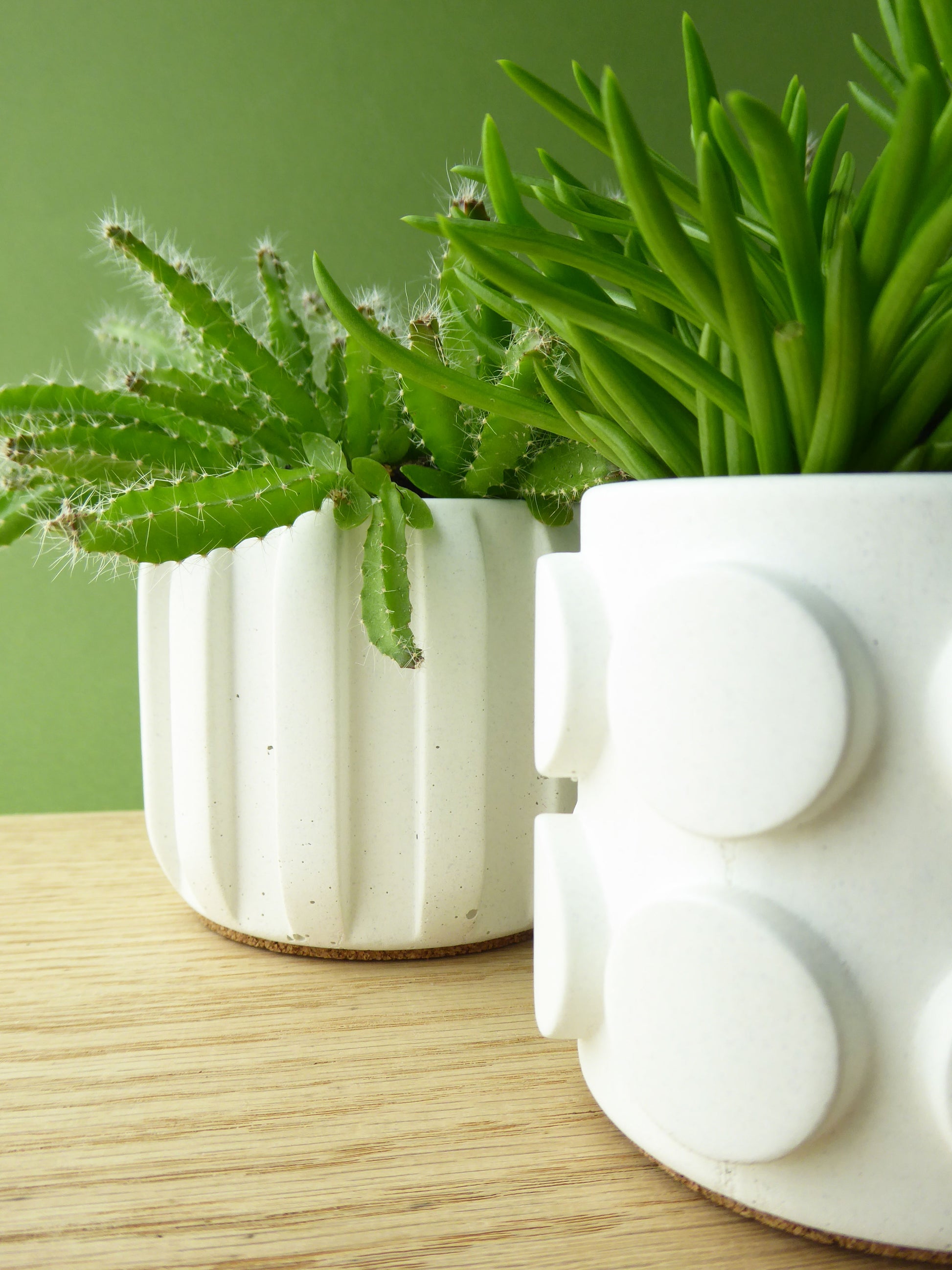 Two white concrete planters with green plants on a wooden shelf.