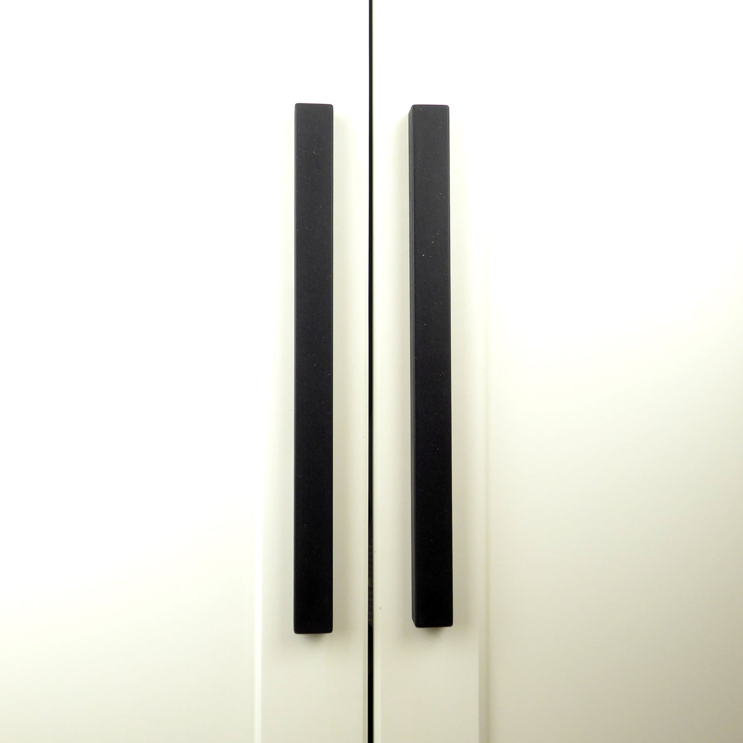 Pair of longline black cupboard door handles on a white kitchen unit