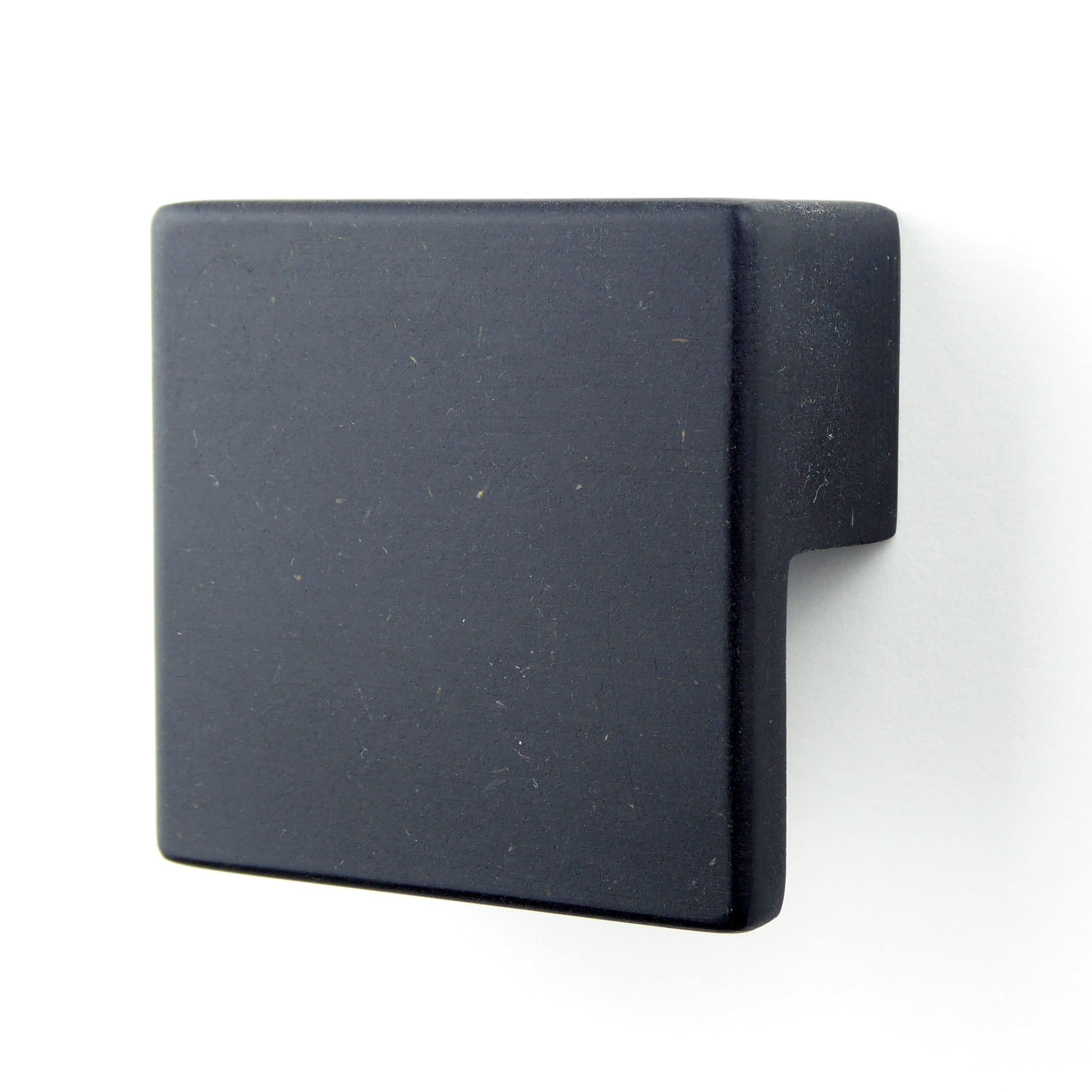 A black square wooden drawer pull handle mounted on a white cabinet