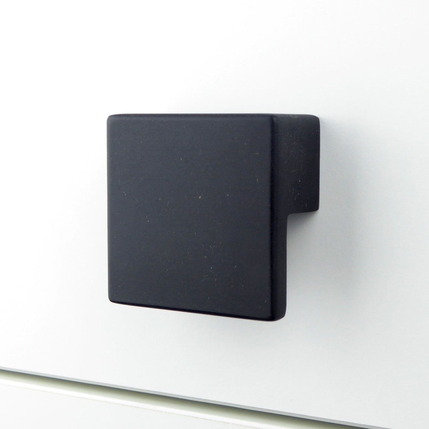 Handcrafted square black drawer pull mounted on a white chest of drawers