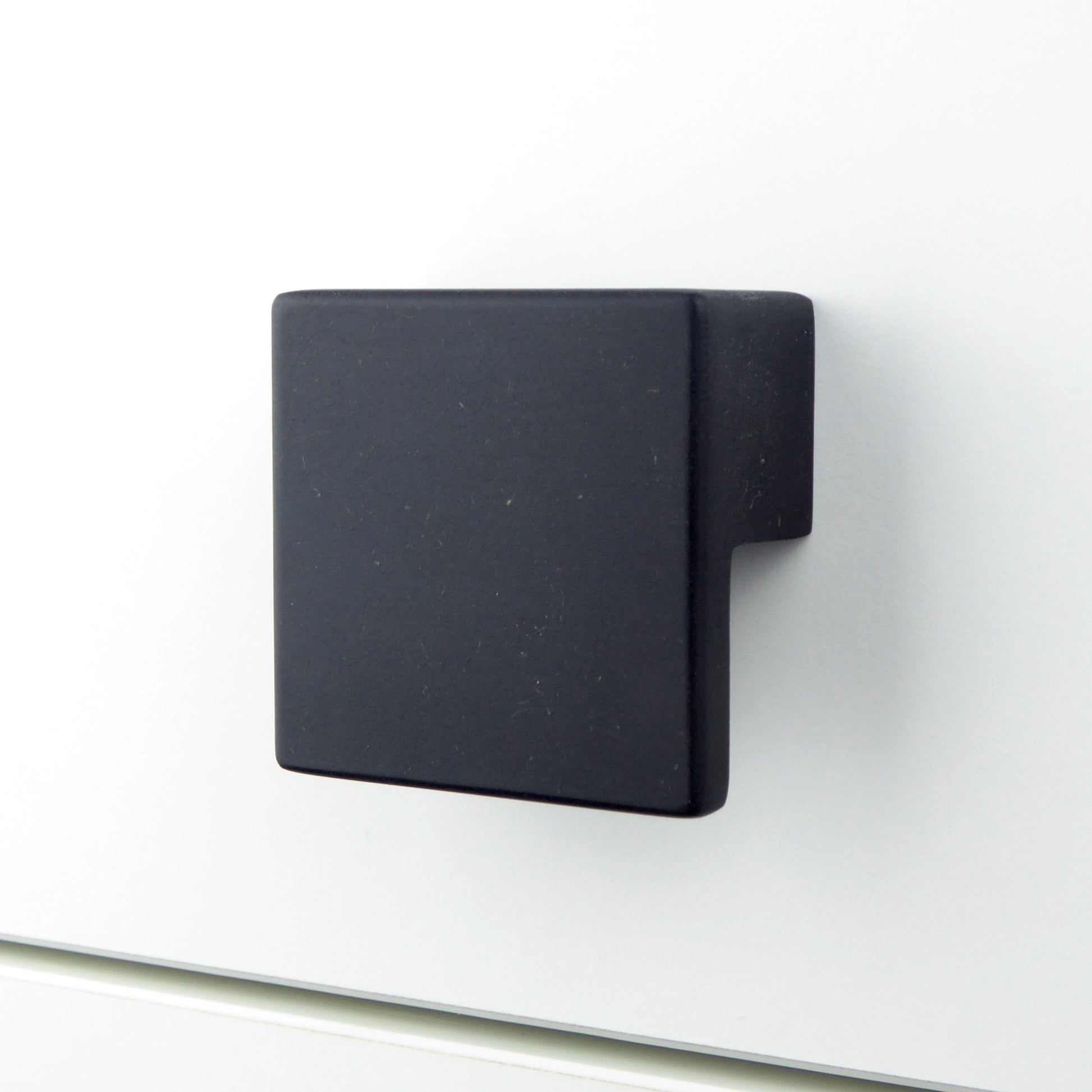 Handcrafted square black drawer pull mounted on a white chest of drawers