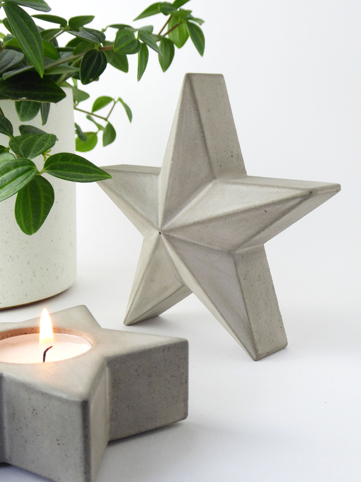 Concrete decorative star and star shaped candle holder with a lit candle on a white background