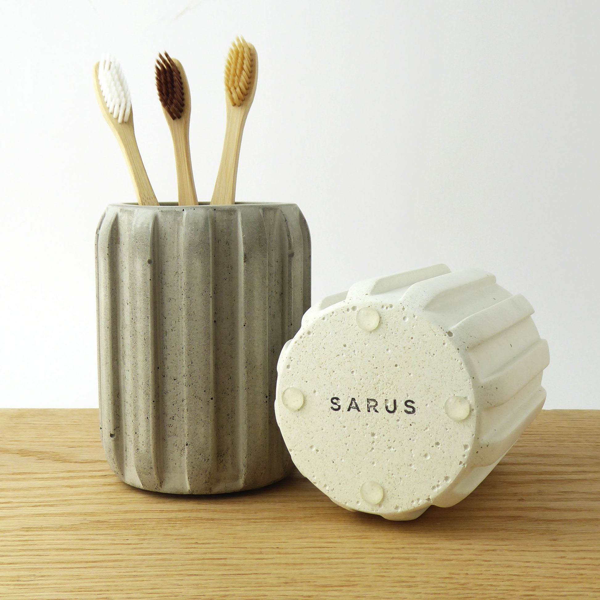 Ceramic toothbrush holder with bamboo toothbrushes and another pot showing the rubber feet to protect surfaces.