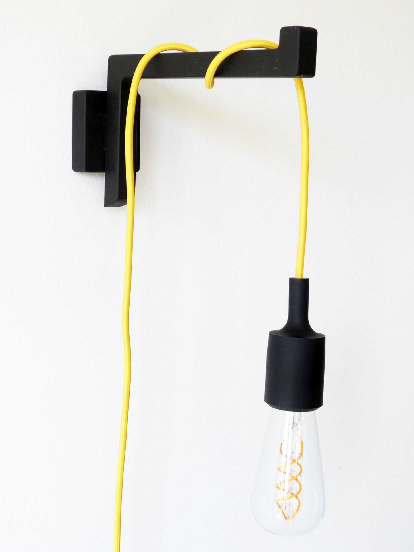 Wall-mounted light bracket with a yellow plug-in pendant cord wrapped around the arm on a white wall