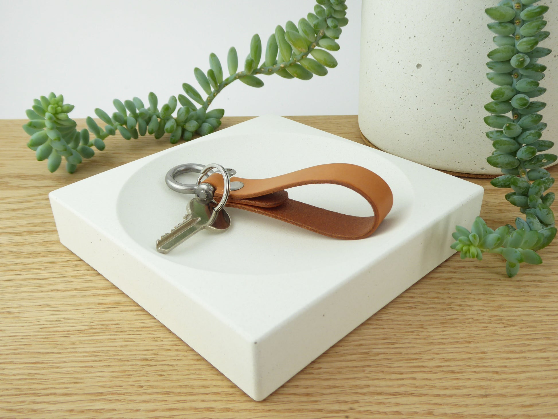 White concrete storage bowl with keys on a hallway table with greenery in the background
