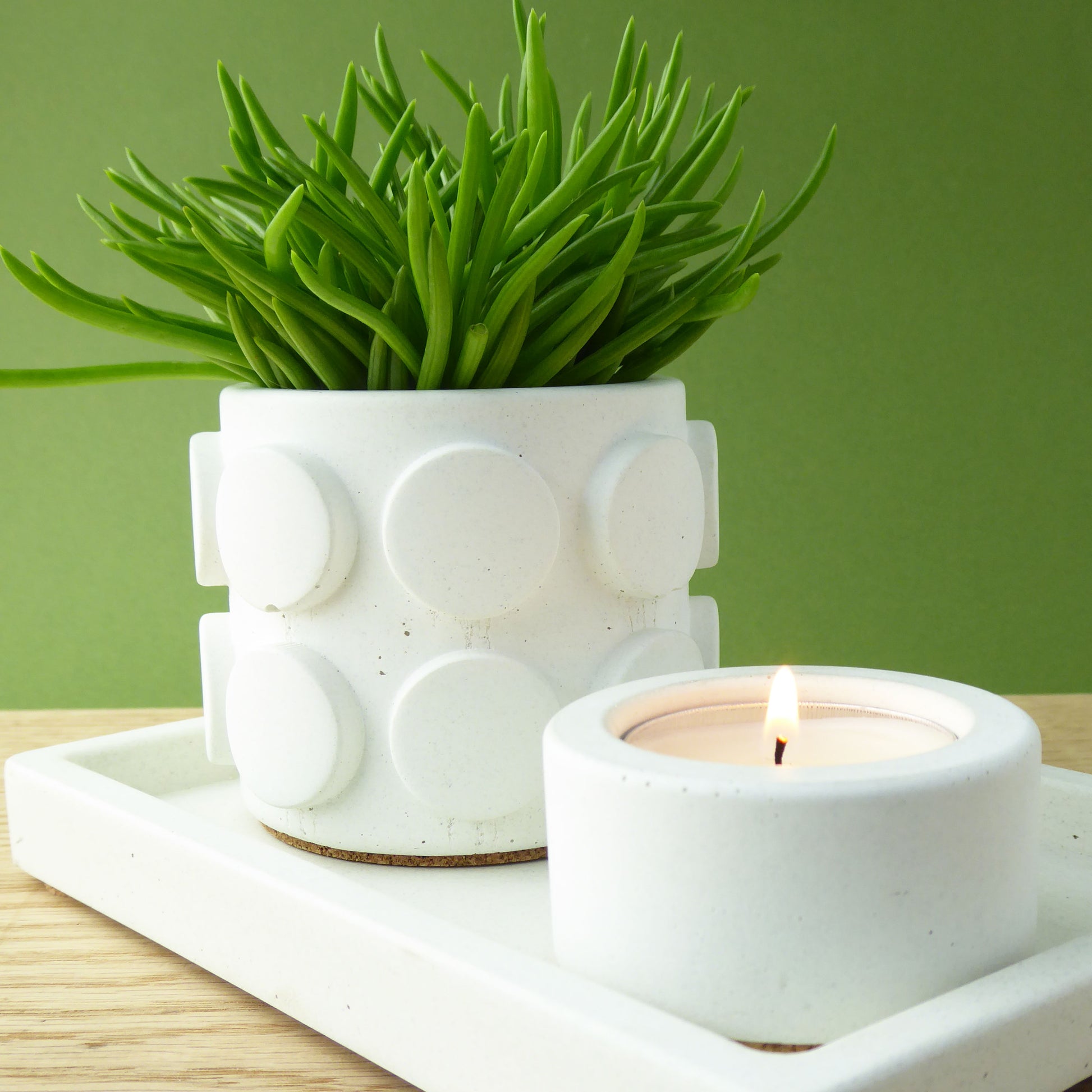 White textured planter with a green succulent plant and a lit white candle on a white concrete tray sitting on a wooden shelp