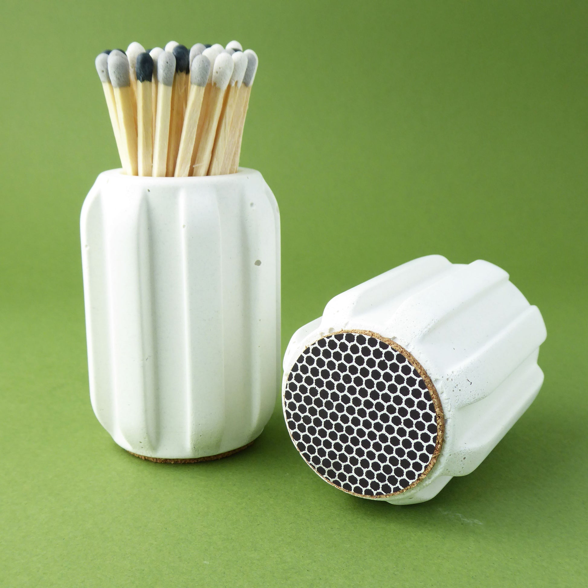 Scandinavian style white concrete match holder with long coloured matches on a green background